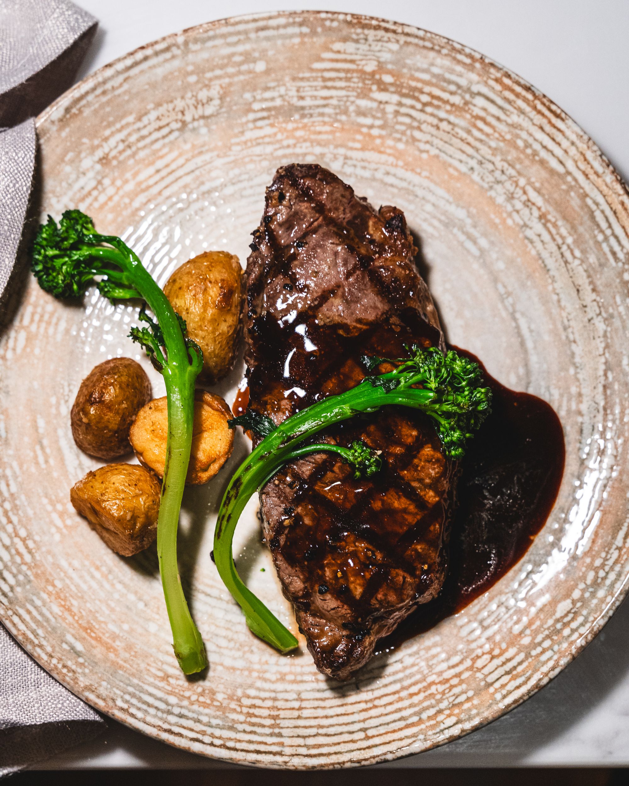 Top down shot of porterhouse steak with potato, broccolini and port jus