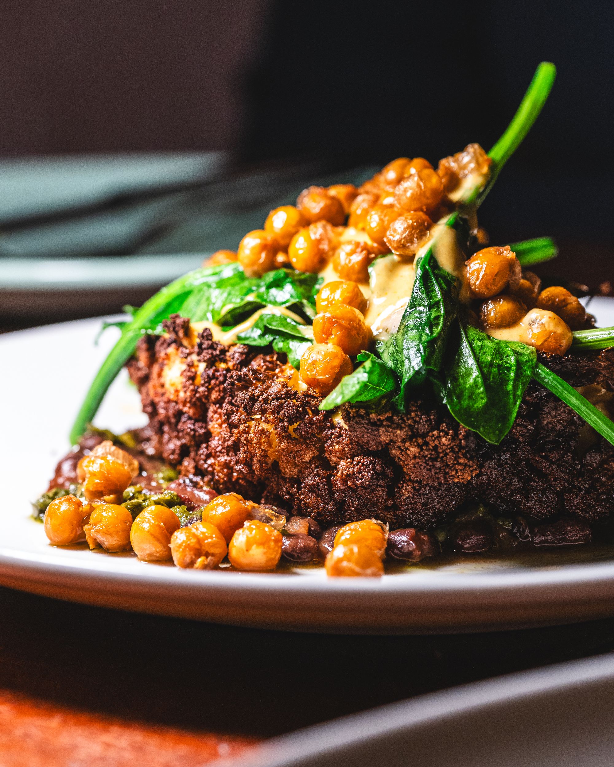 Close of up entire roasted cauliflower head, chickpeas and spinach