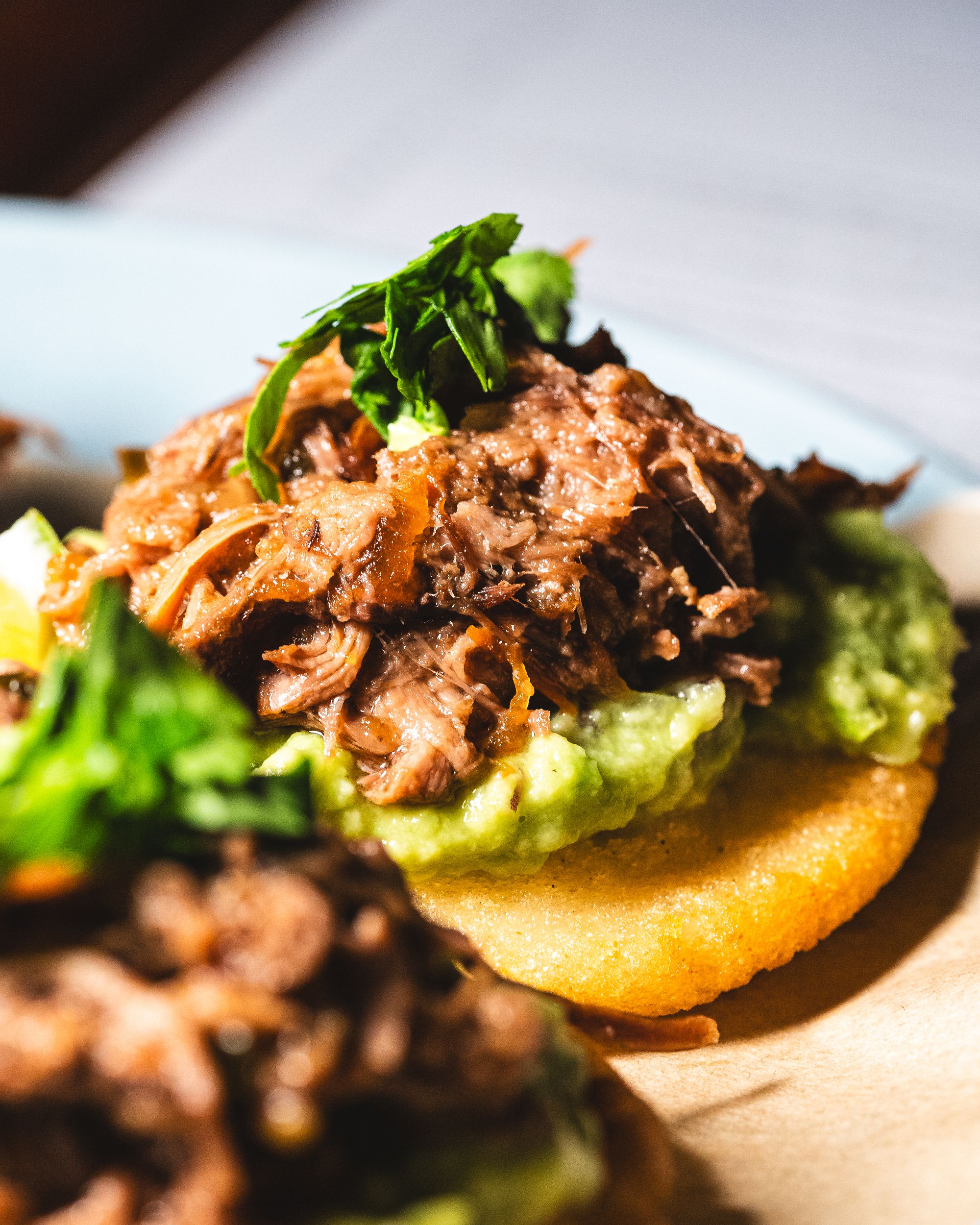 Close up of braised ox tail on an arepa with aji and salsa