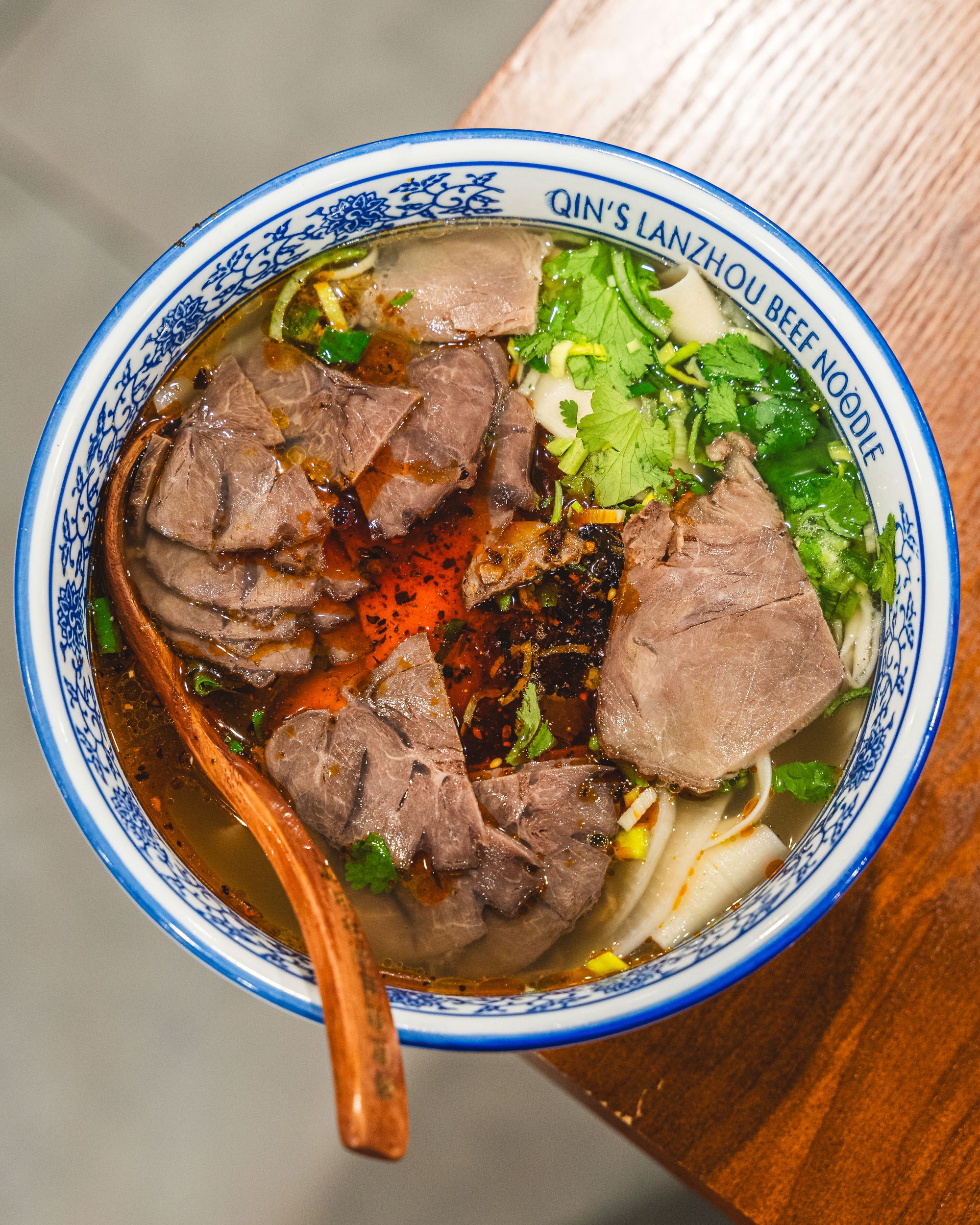 Top down shot of a bowl of noodles, beef slices, coriander and chilli oil