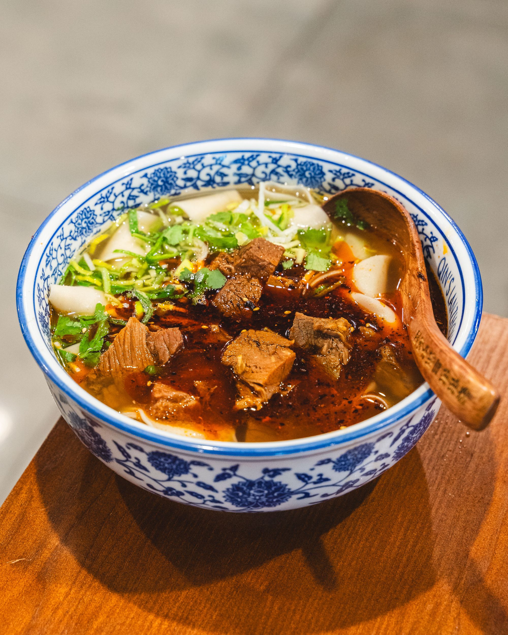 Top down shot of a bowl of noodles, beef brisket pieces, coriander and chilli oil