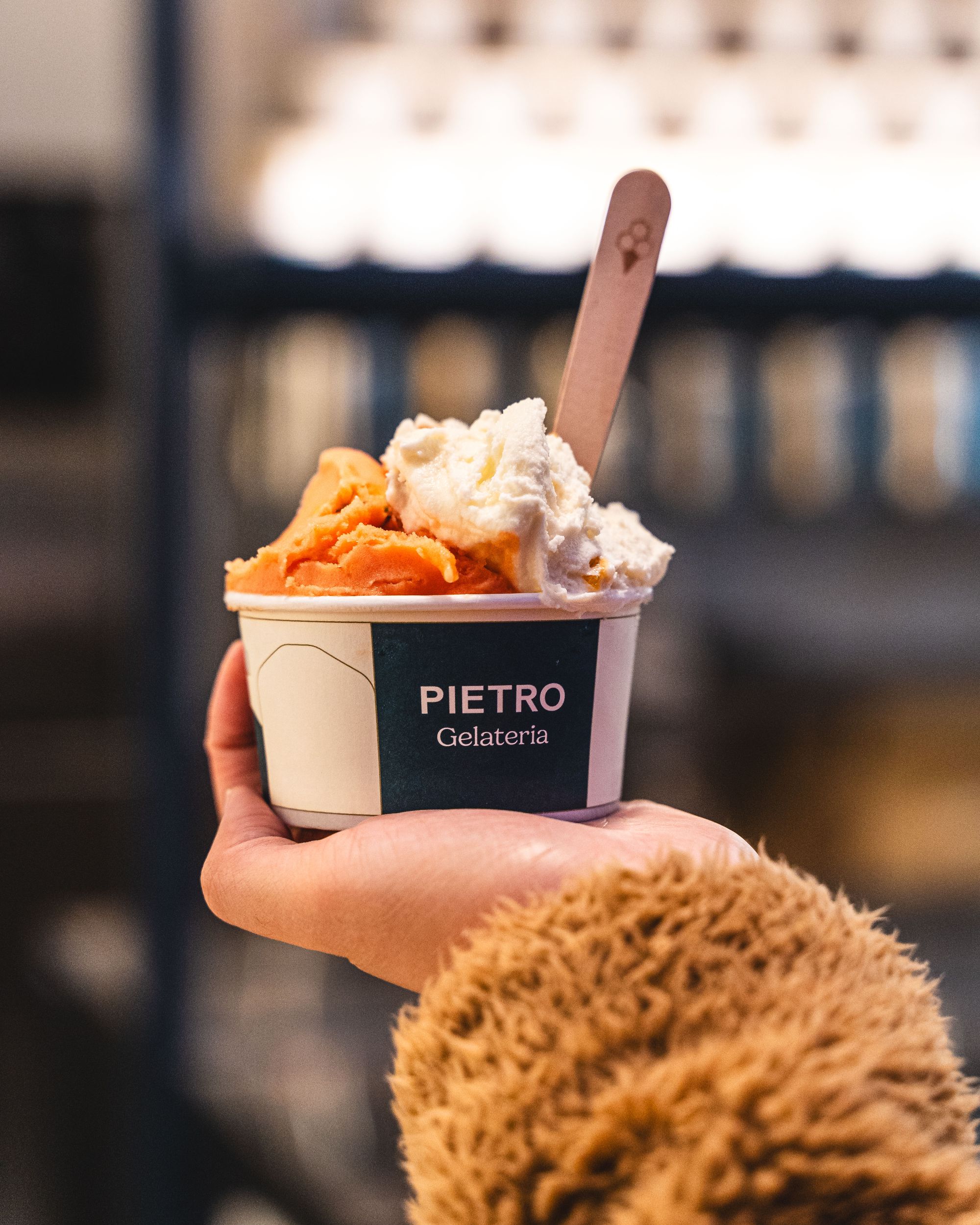 Hand holding up a cup of gelato with a spoon sticking out