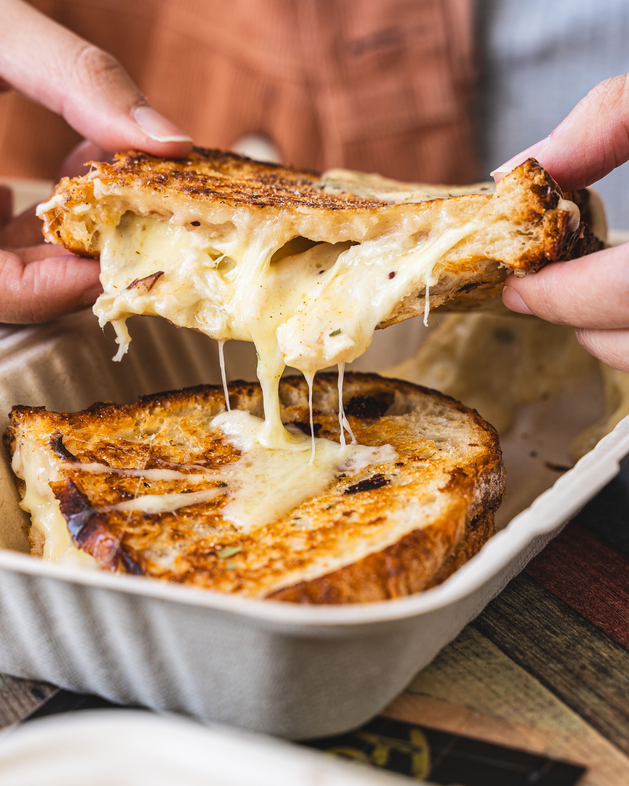 Close up of a hand lifting up a toasted sandwich with cheese oozing out