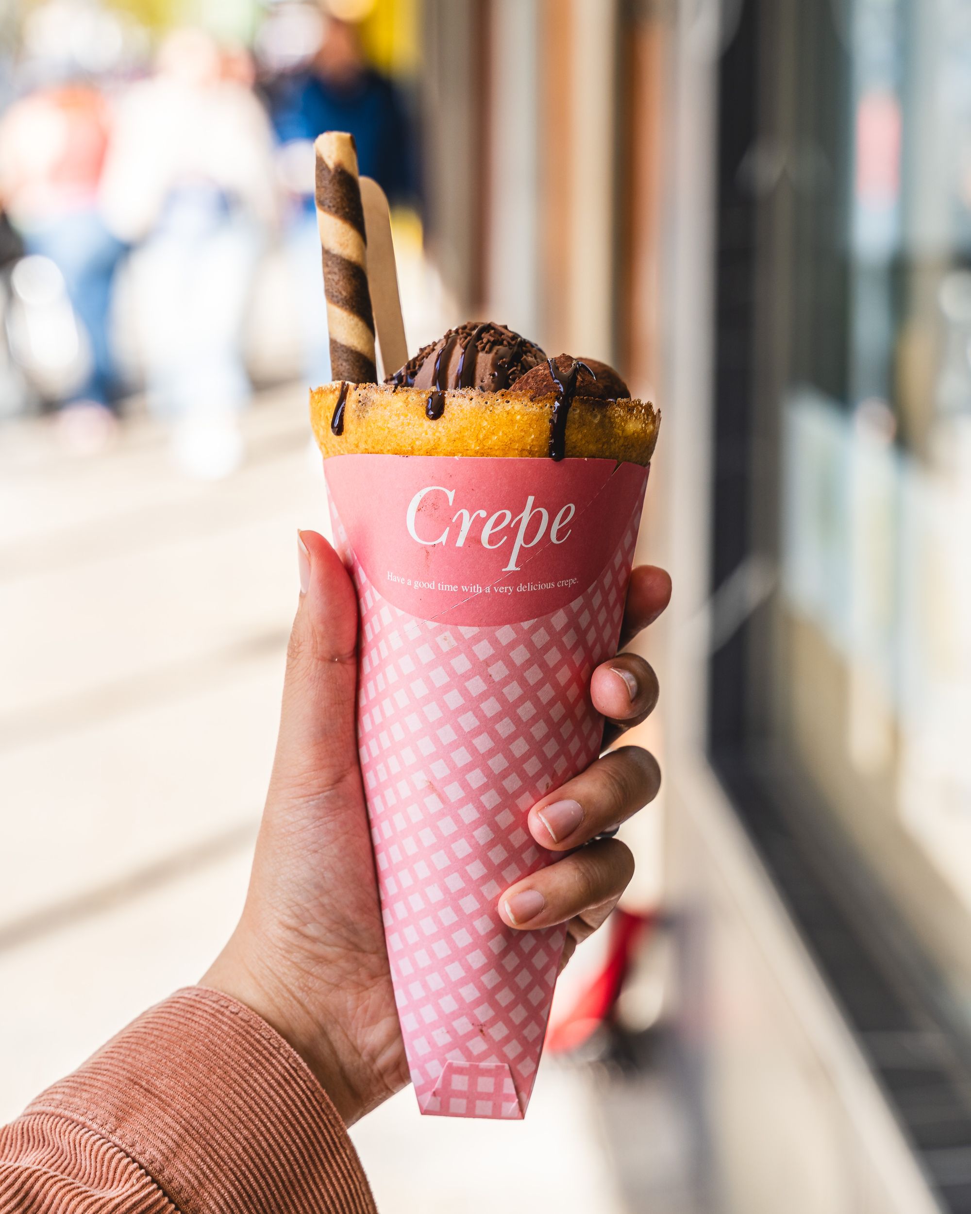 Hand holding a Japanese style crepe with chocolate sauce, ice-cream and a chocolate wafer