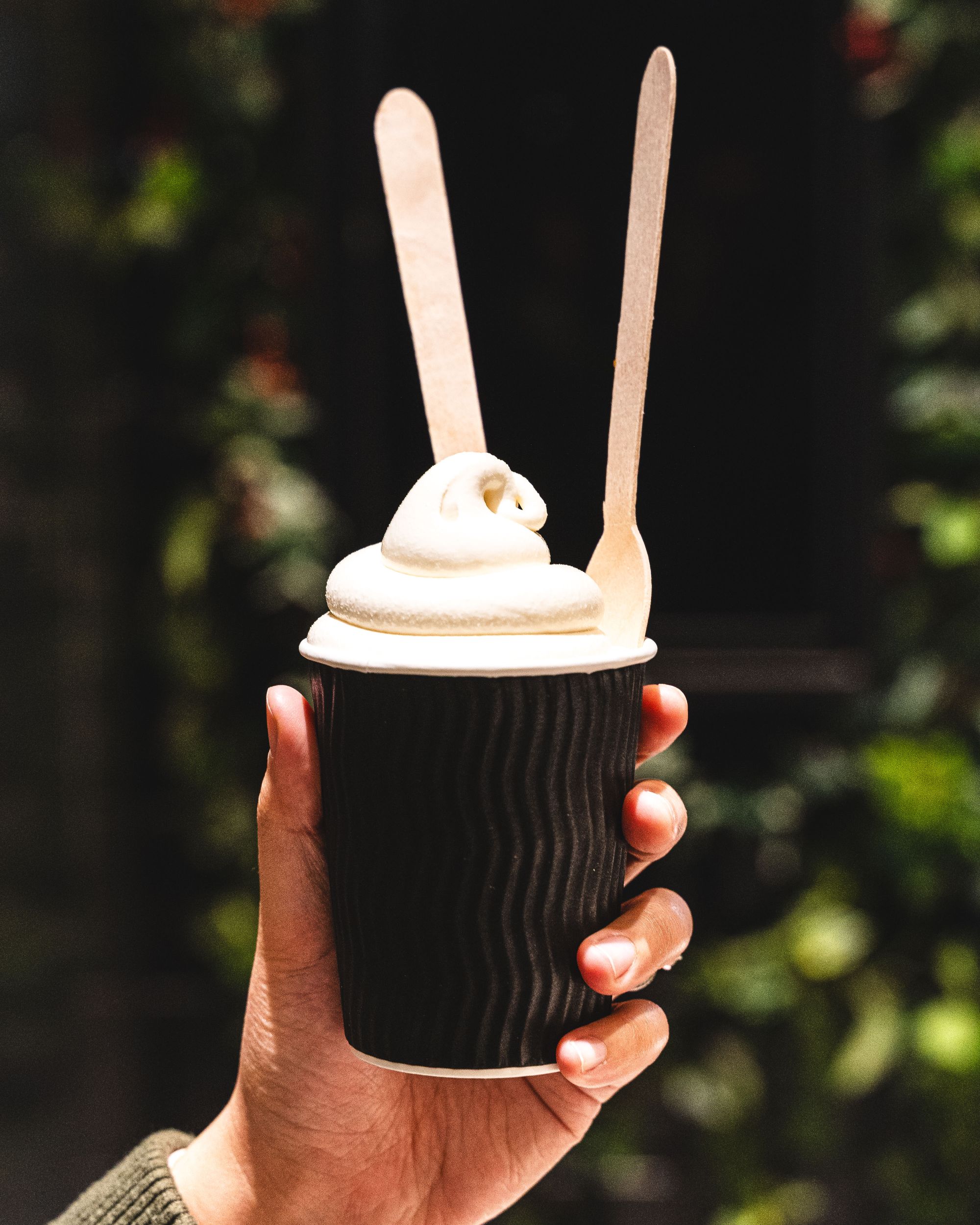 Hand holding a cup with soft serve and two spoons sticking out