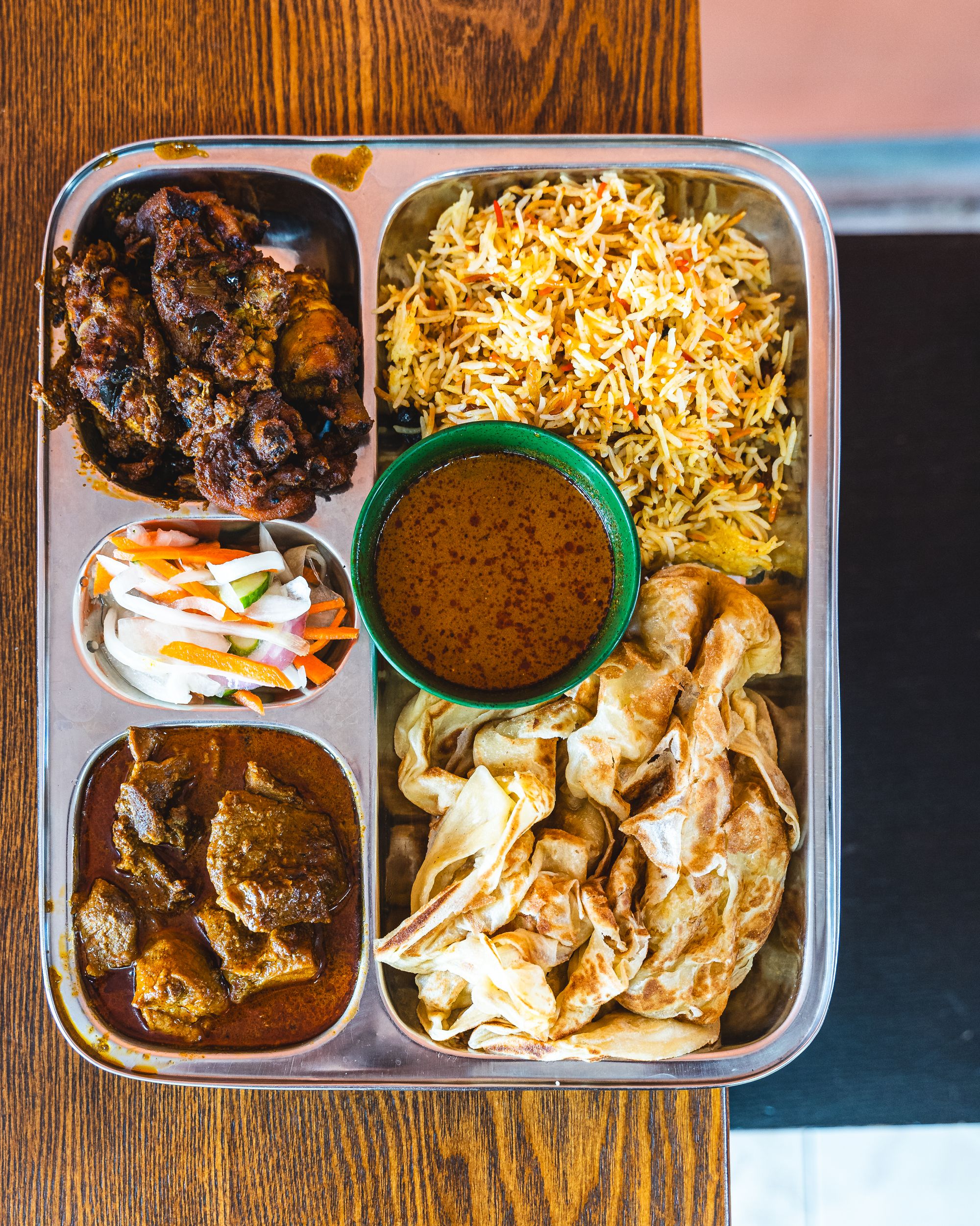 Top down of curry on a silver tray with roti and briyani