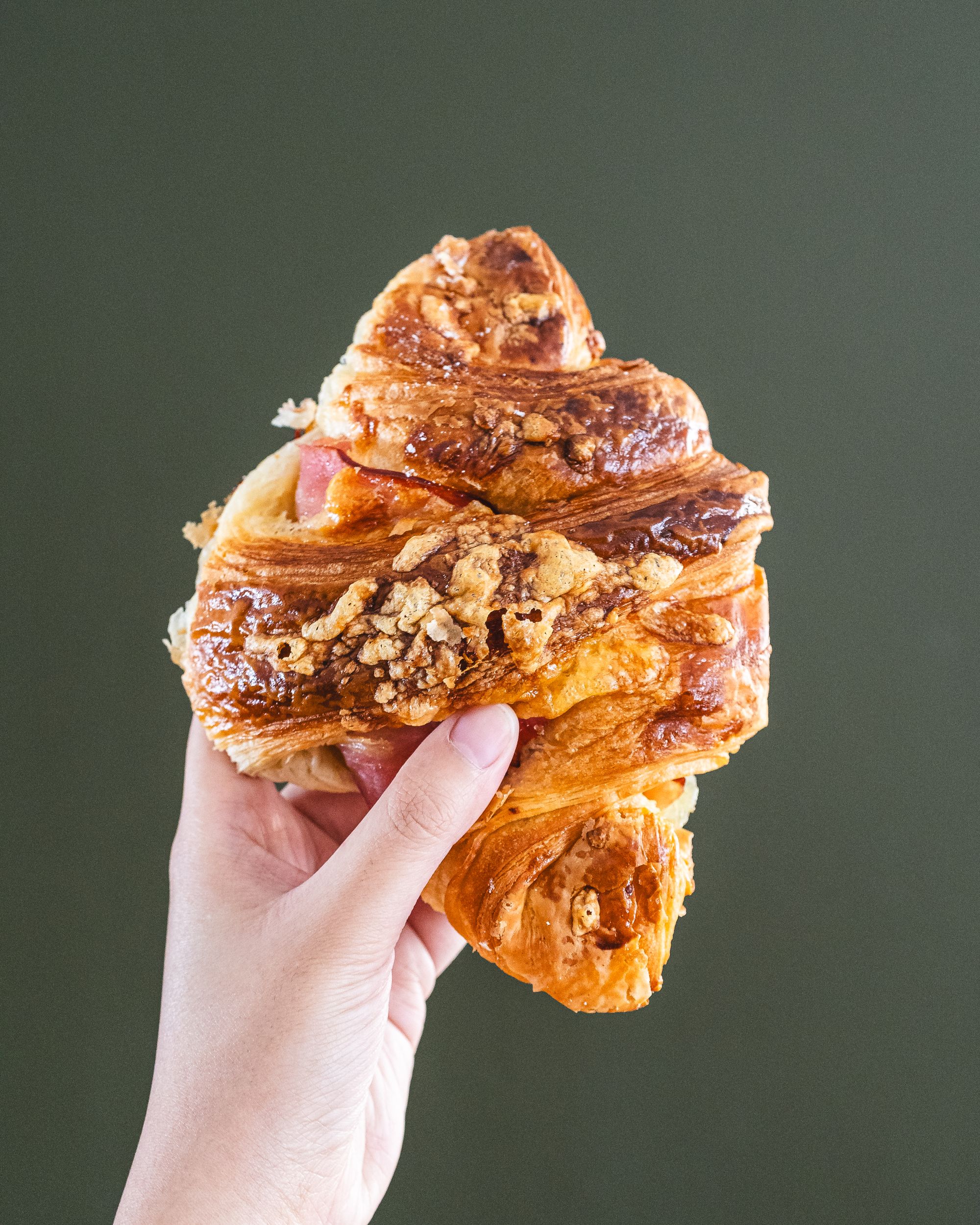 Hand holding croissant against green background