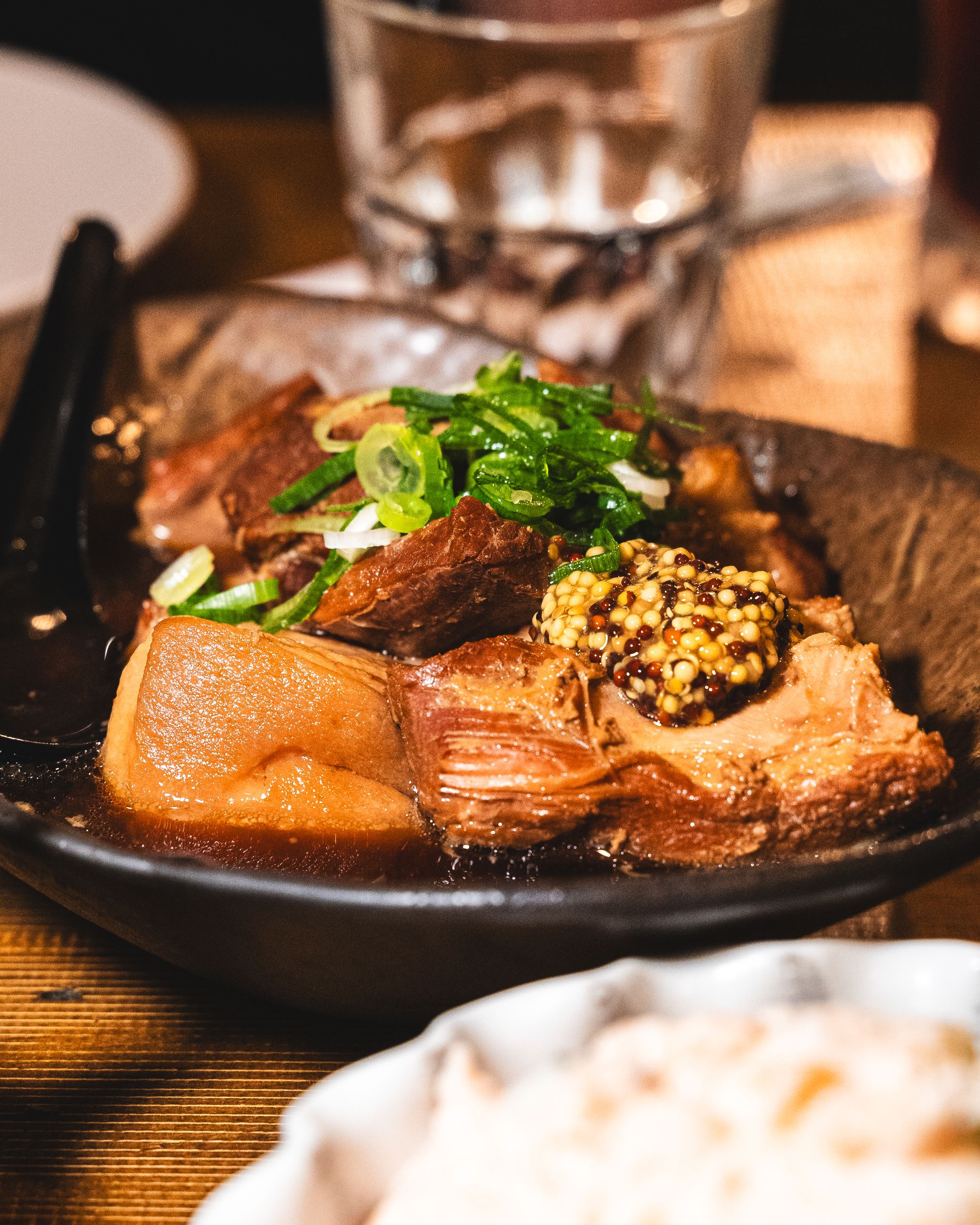 Close up of pork kakuni with spring onions and mustard as garnish 