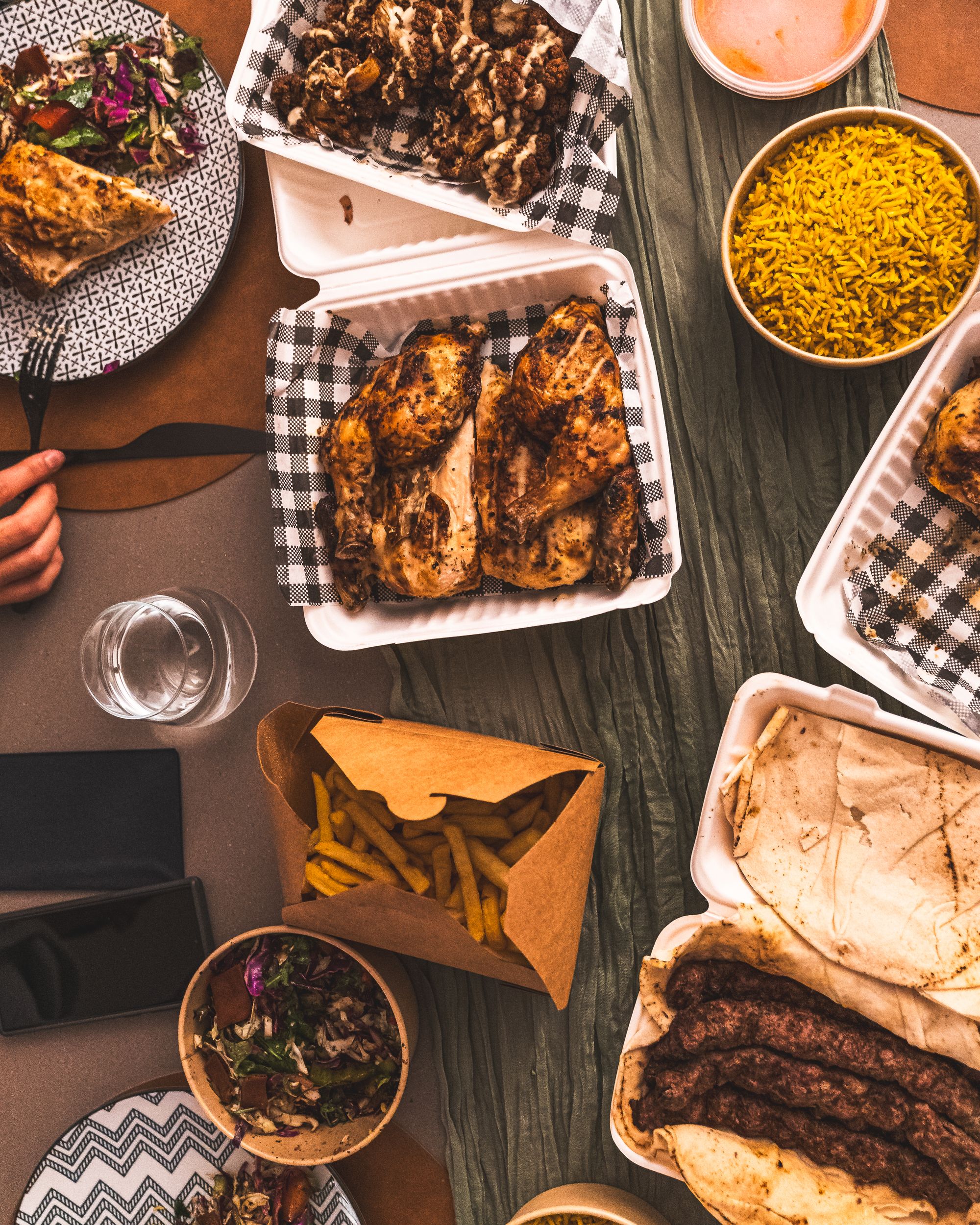 Top down shot showing a spread of charcoal chicken, chips, salad, rice and koftas