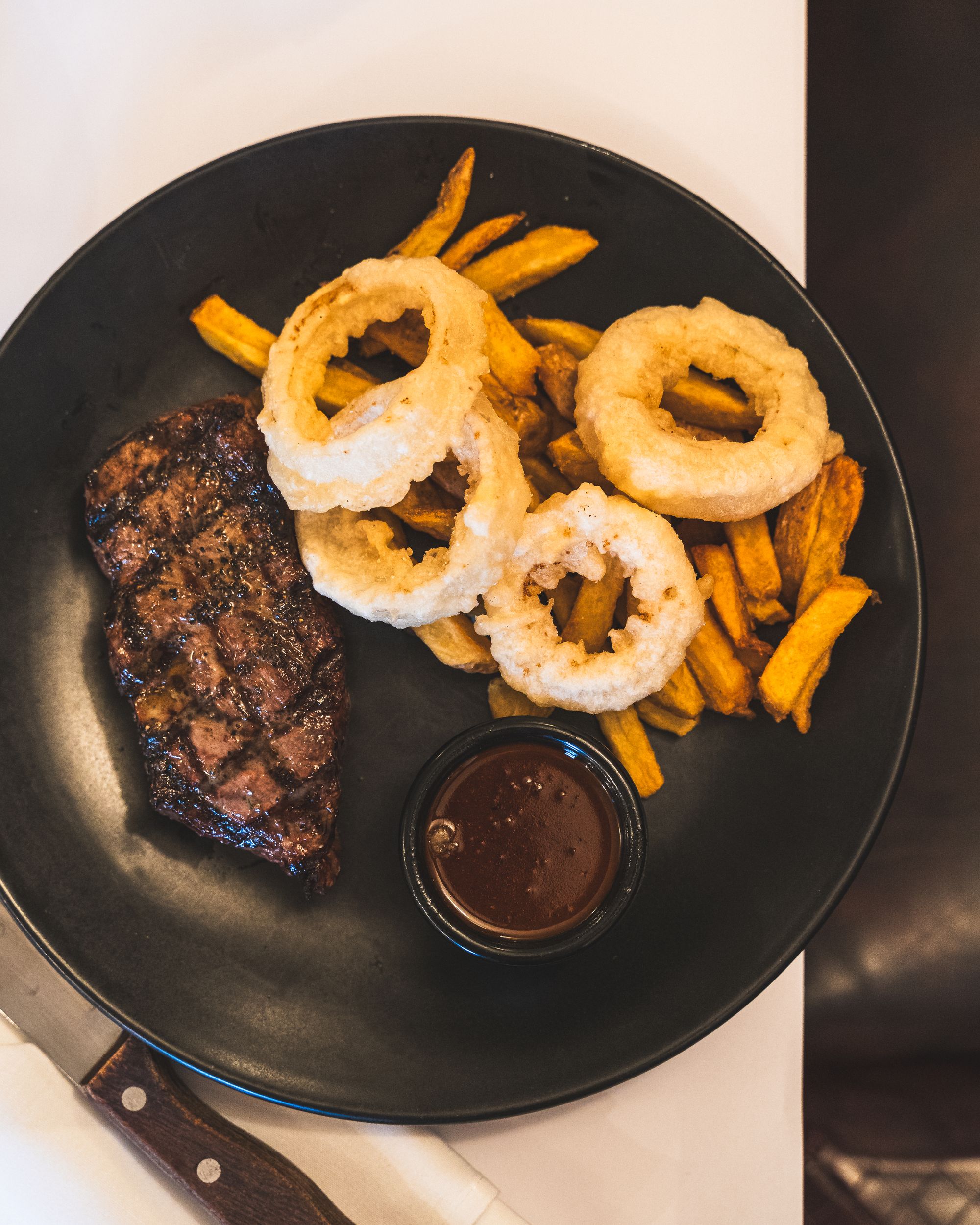 Top down shot of steak with grill marks on a plate with chunky chips, onion rings and mushroom sauce