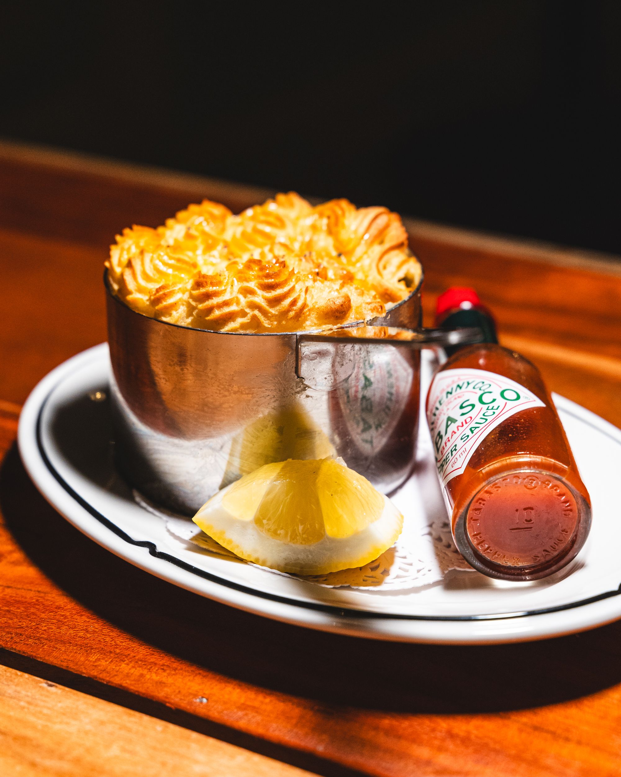 Close up of potato top pie with lemon wedge and a bottle of tabasco sauce on side