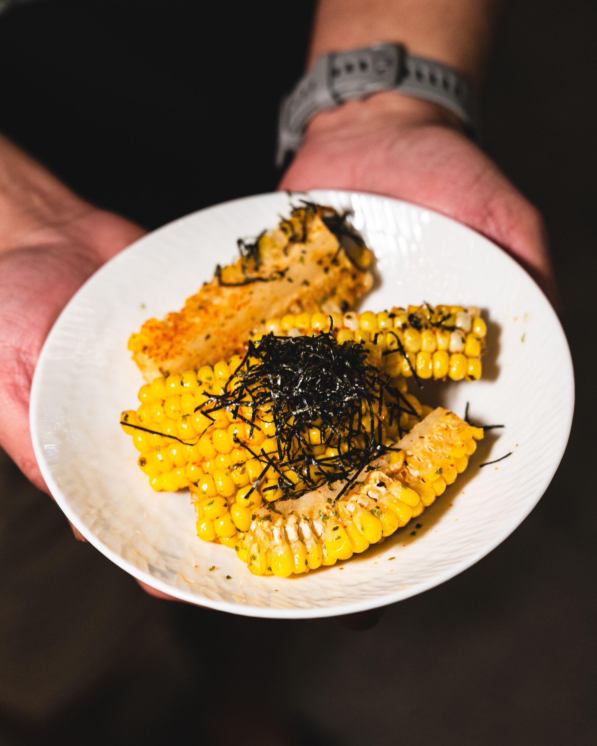 Hand holding corn ribs topped with seaweed