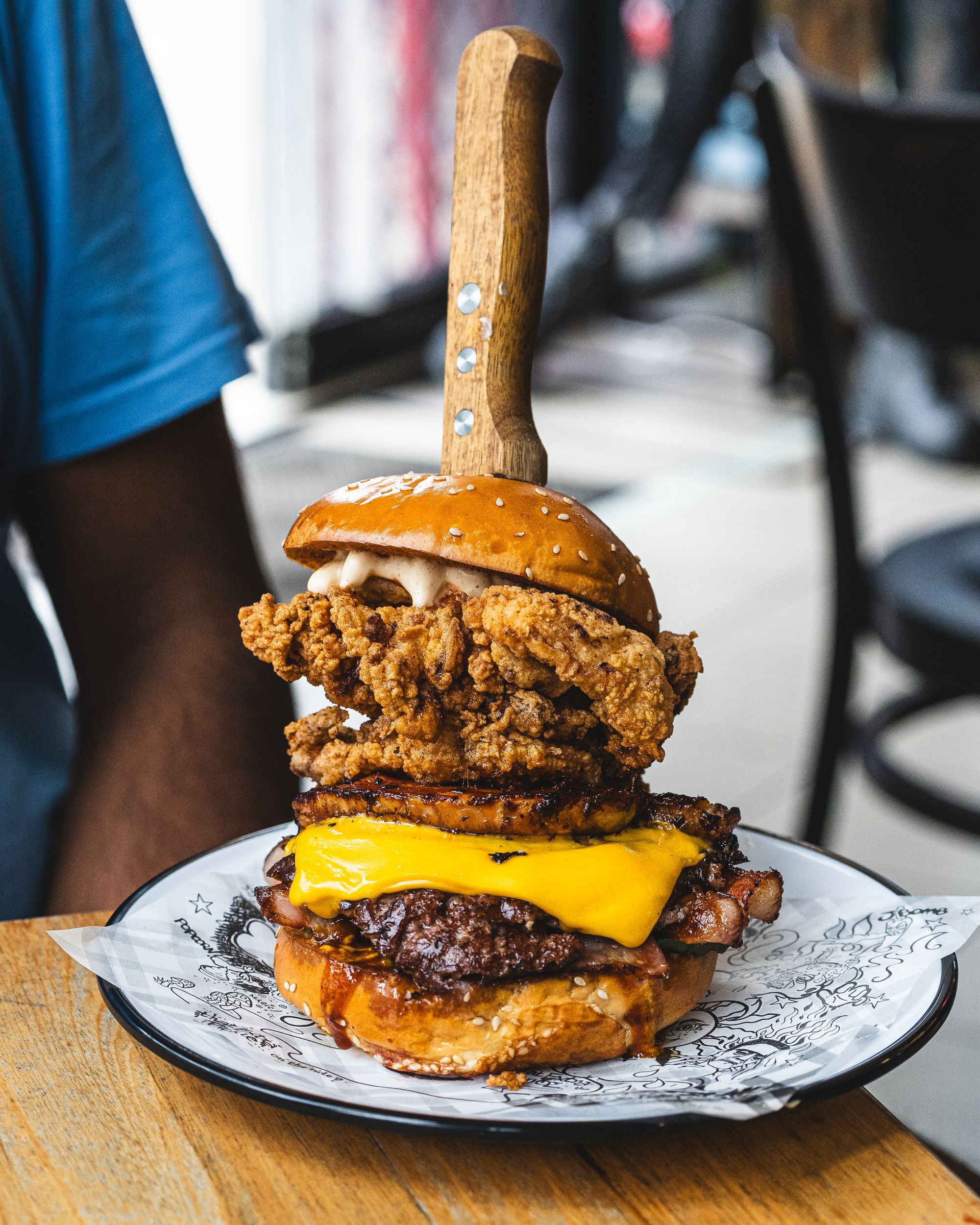 Large burger with fried chicken, melted cheese and bacon with a steak knife holding it together