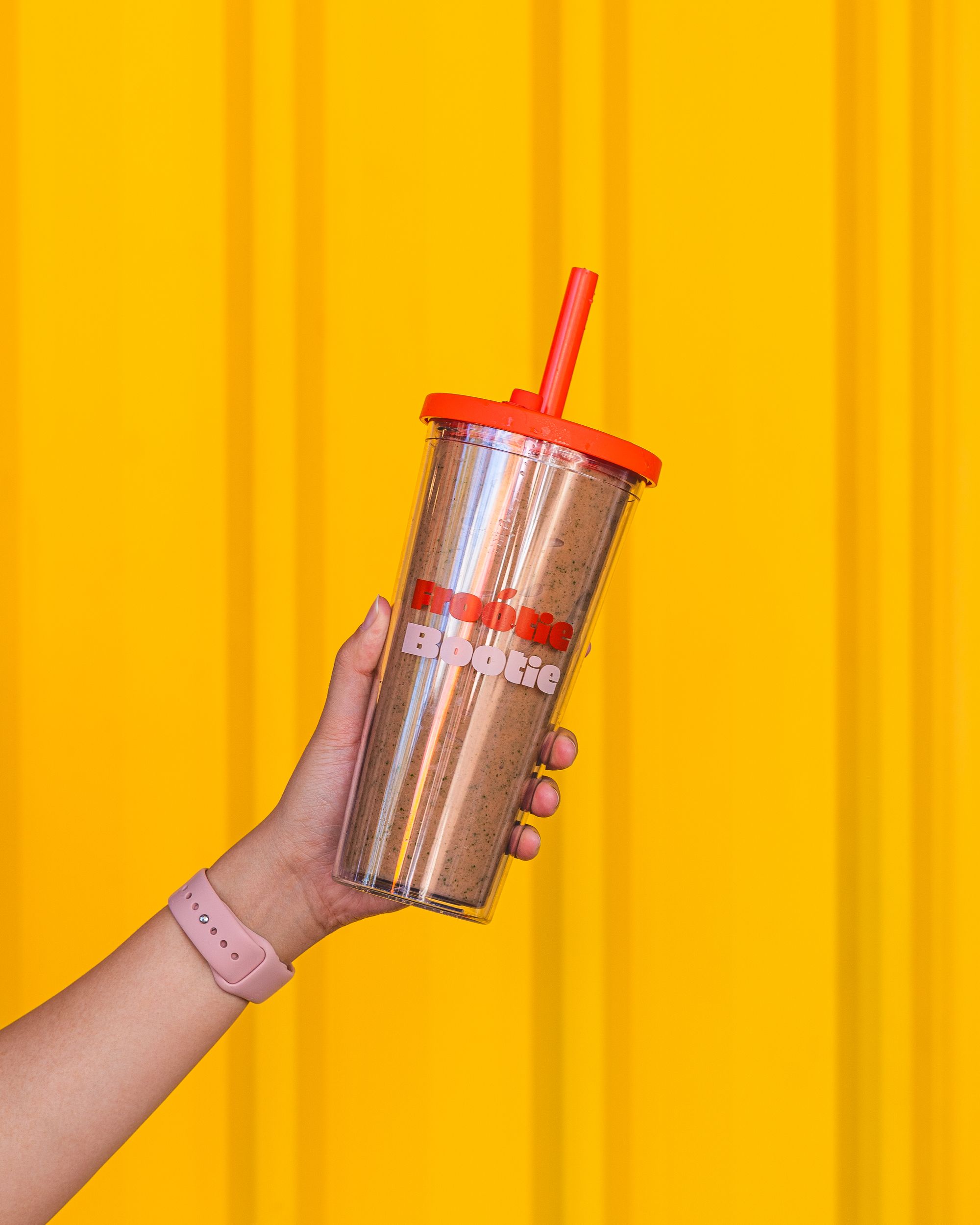 Hand holding a smoothie in a re-usable plastic cup.