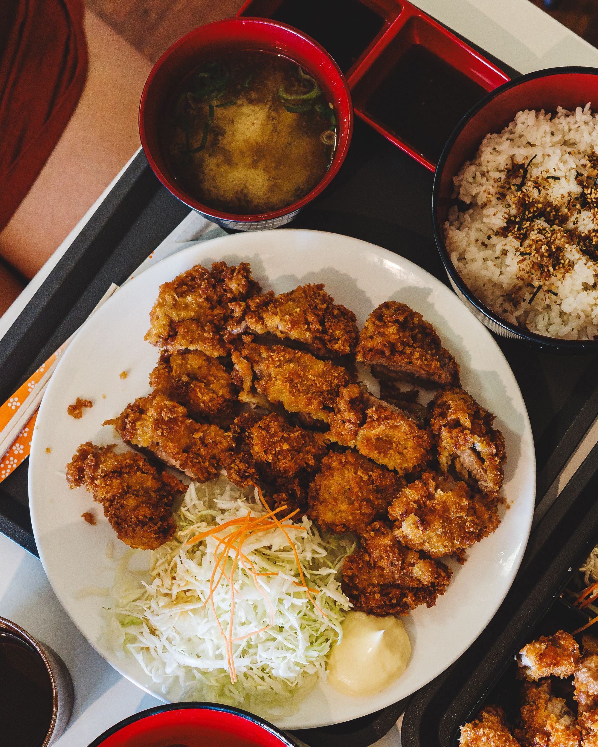 Top down shot of pork katsu on rice with salad, miso soup and gyoza