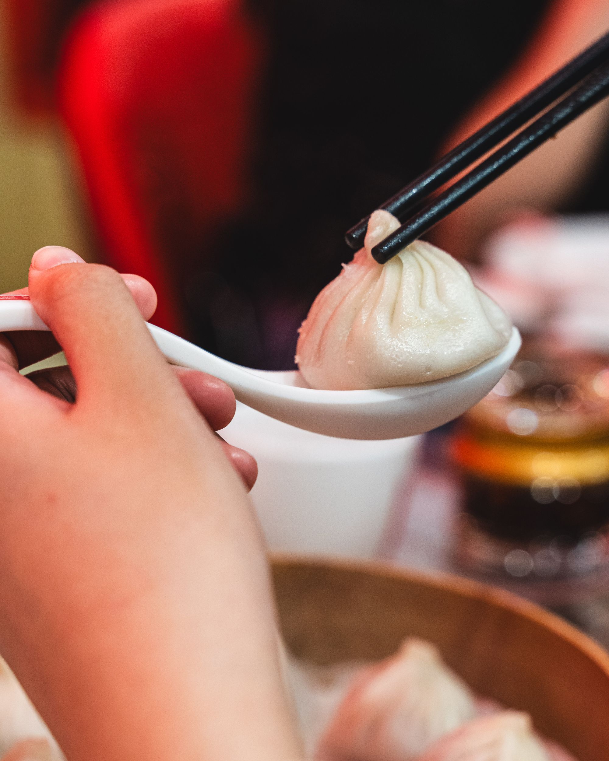 Close up of xiao long bao on a soup spoon being picked up with chopsticks