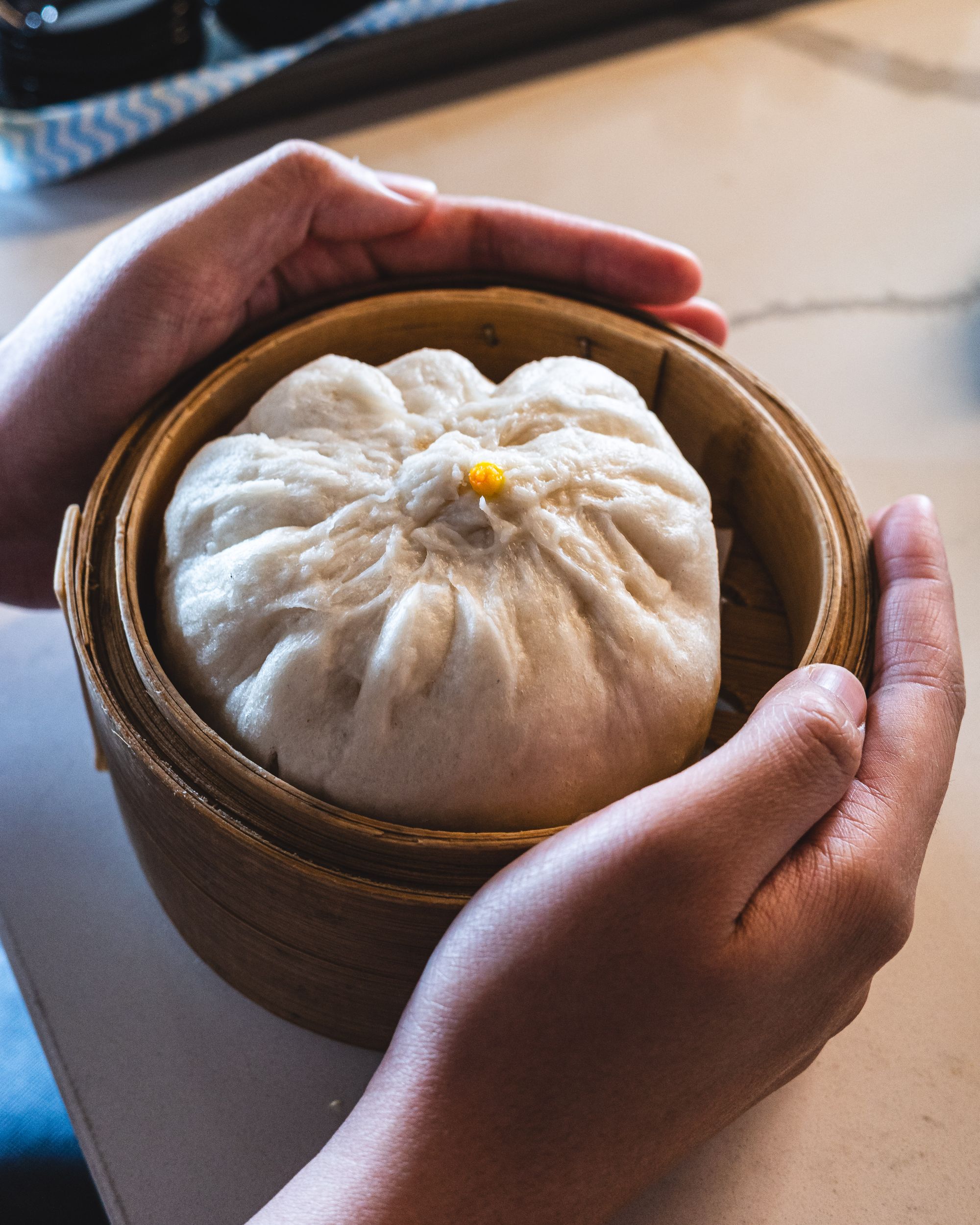 Hands holding a bamboo steamer basket with a large bao inside