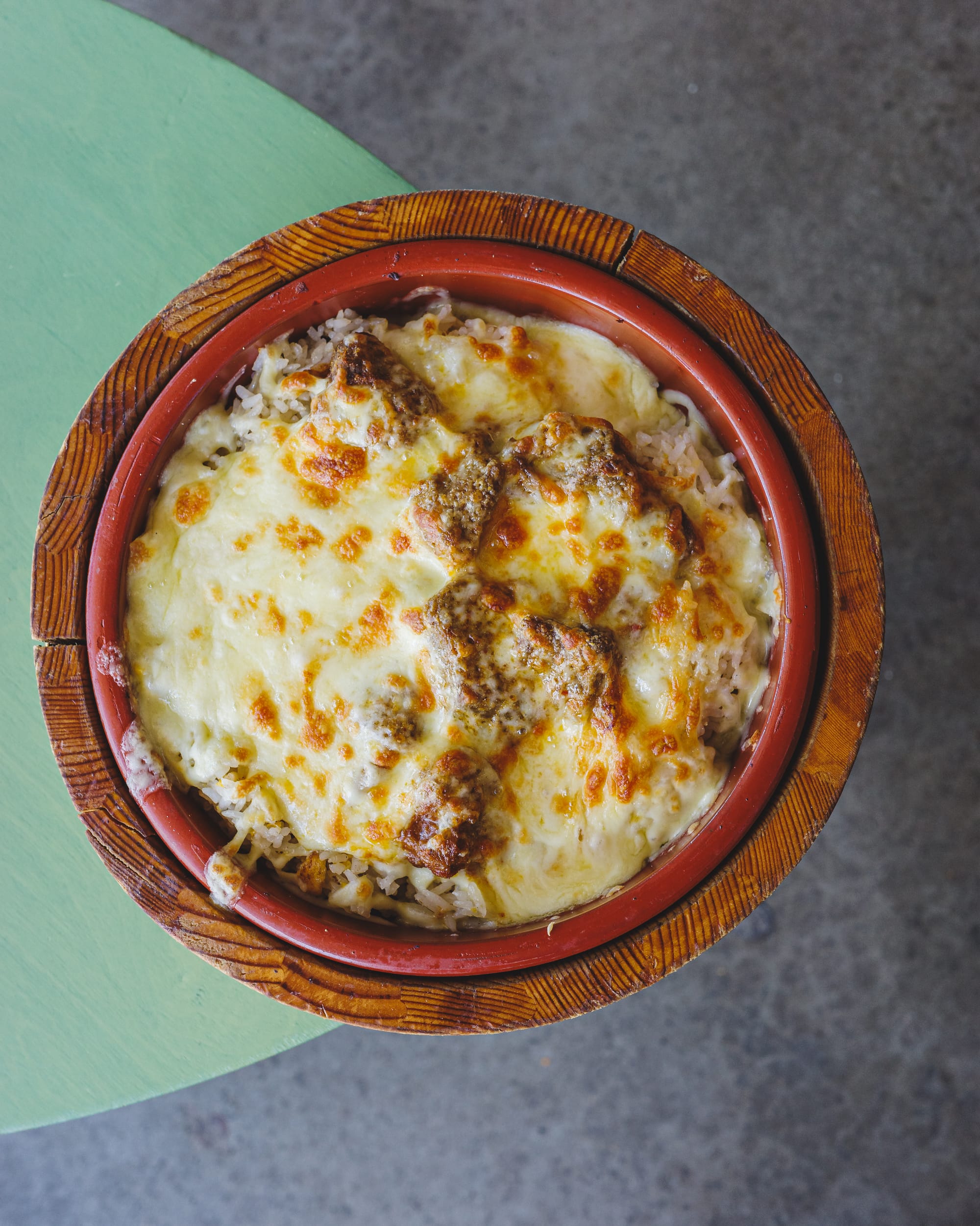 Top down shot of cheese melted on-top of lamb rendang on a circular plate