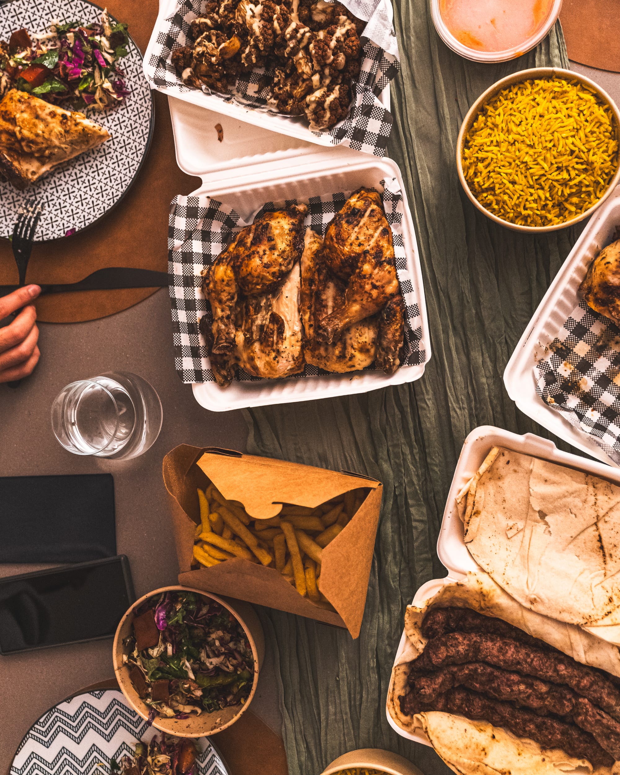 Flatlay of charcoal chicken in a takeaway container, chips, beef koftas, rice