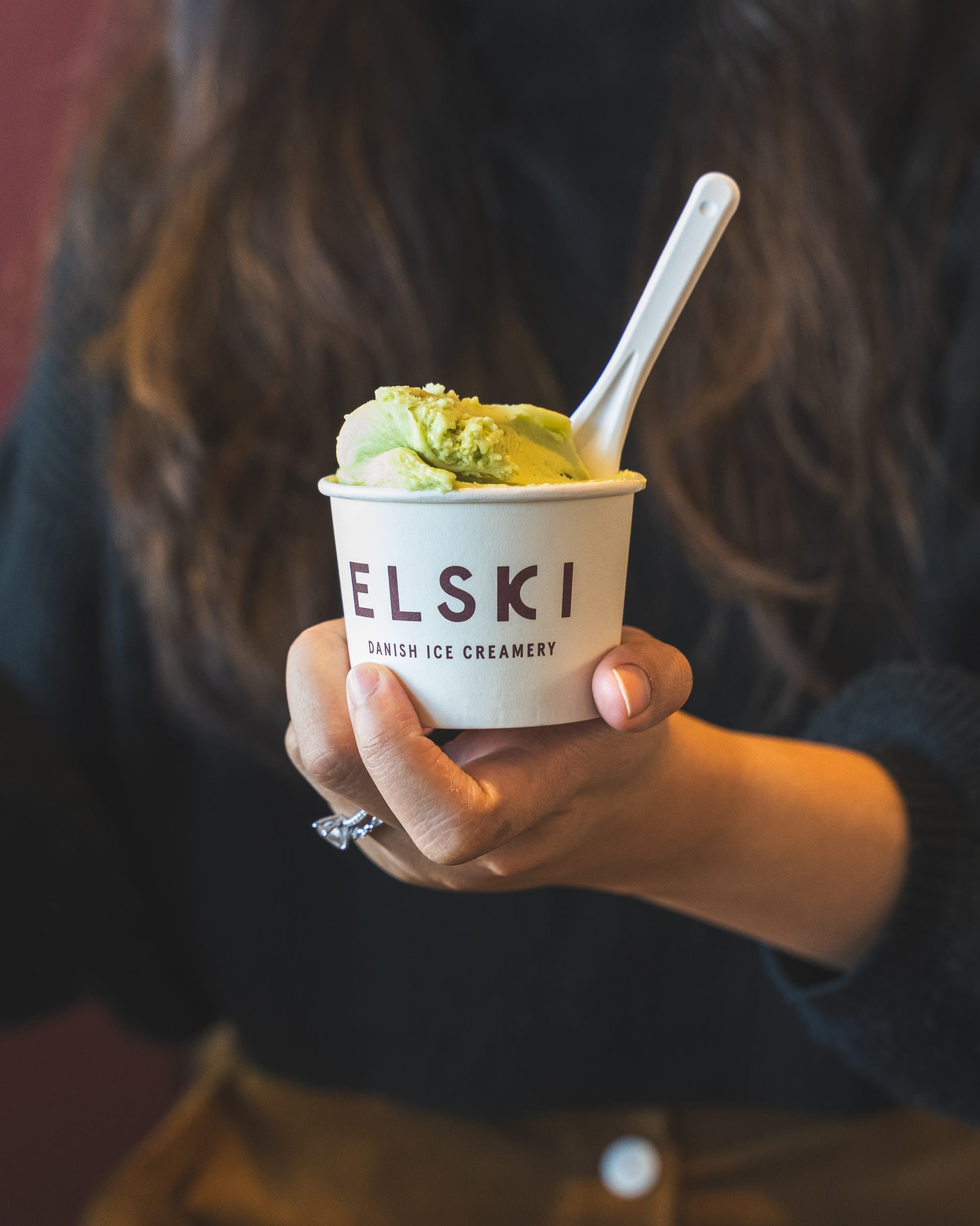 Hand holding a cup with "Elski Danish Ice Creamery" on it and a scoop of ice-cream