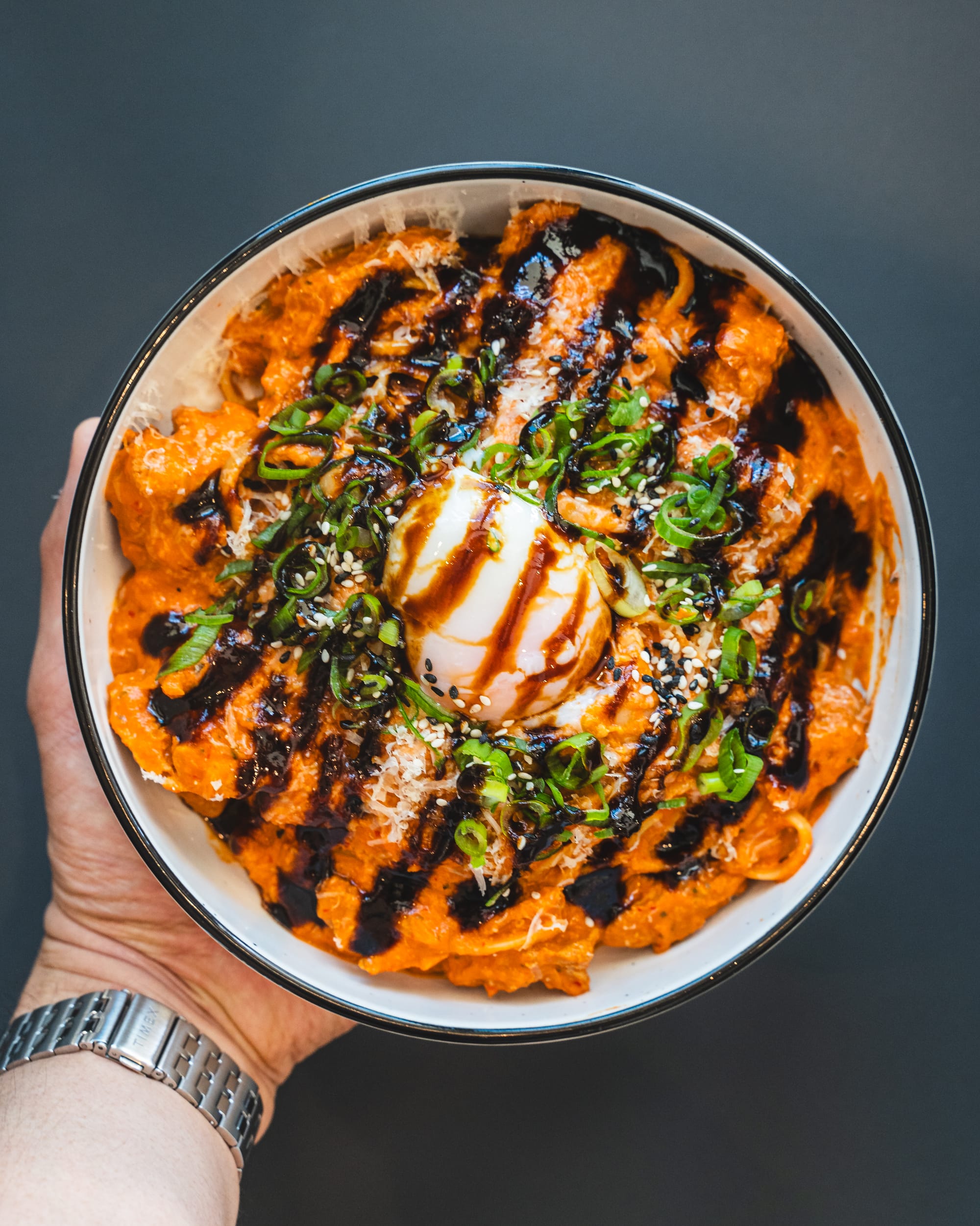 Hand holding a bowl of pasta with a sous vide egg and tonkatsu sauce