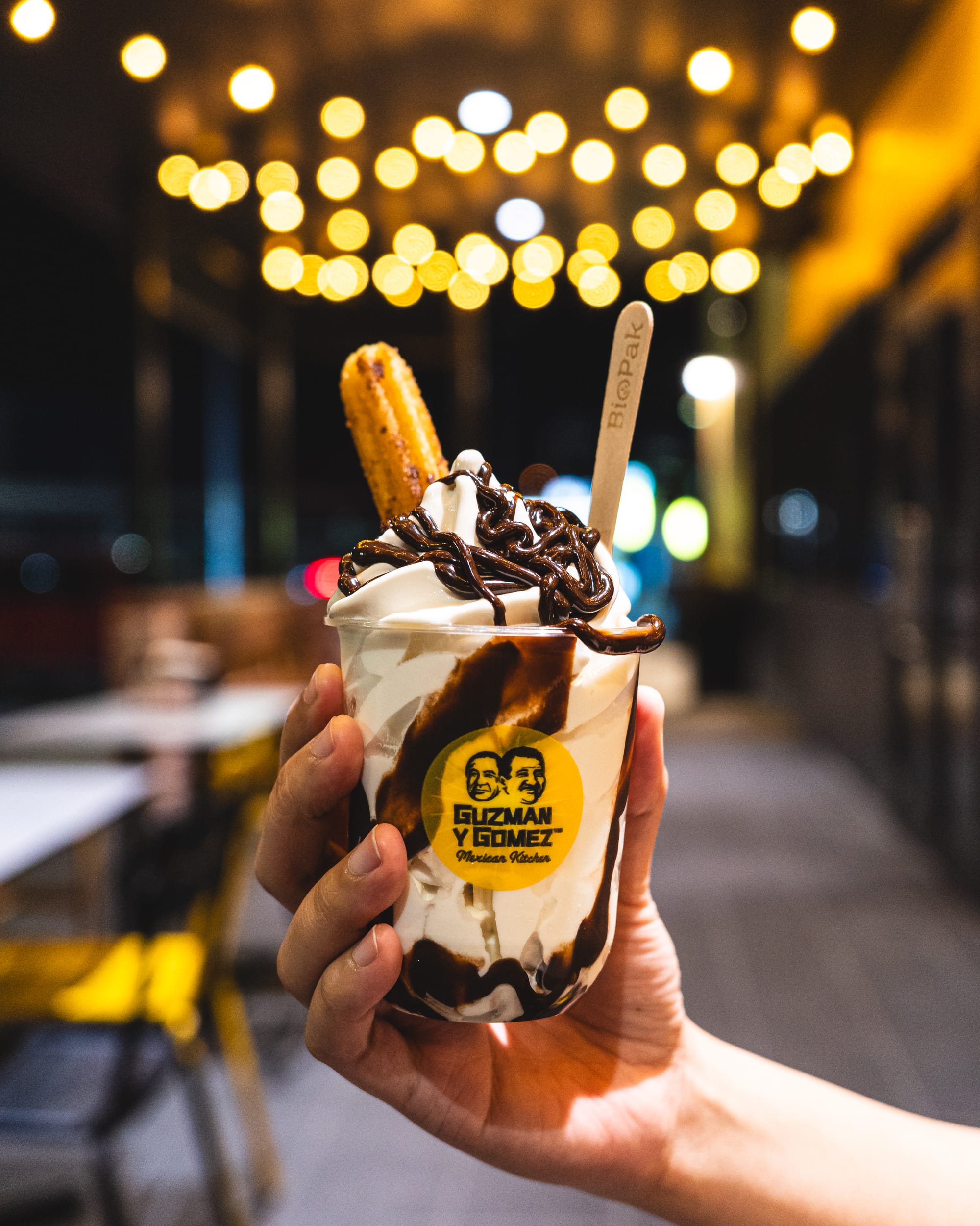 Hand holding soft serve with a churro served in a plastic Guzman y Gomez cup