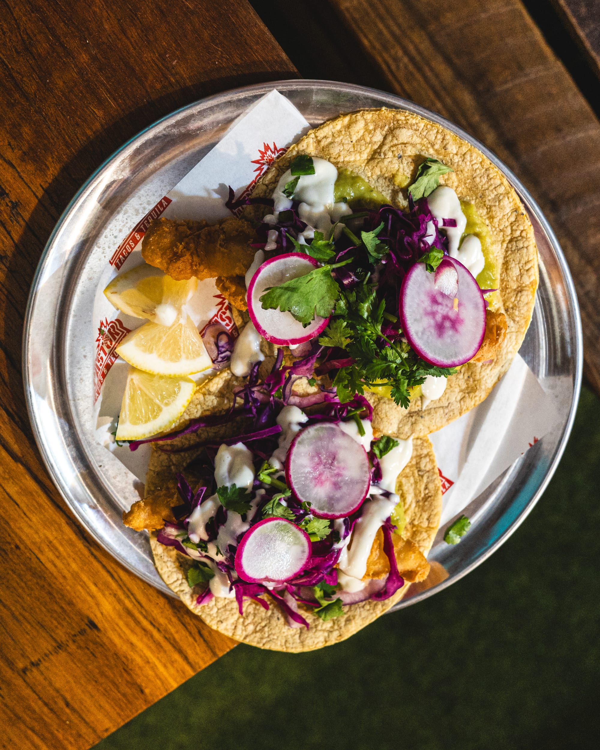 Top down shot of fried fish tacos with guacamole, red cabbage, lime, onion and aioli