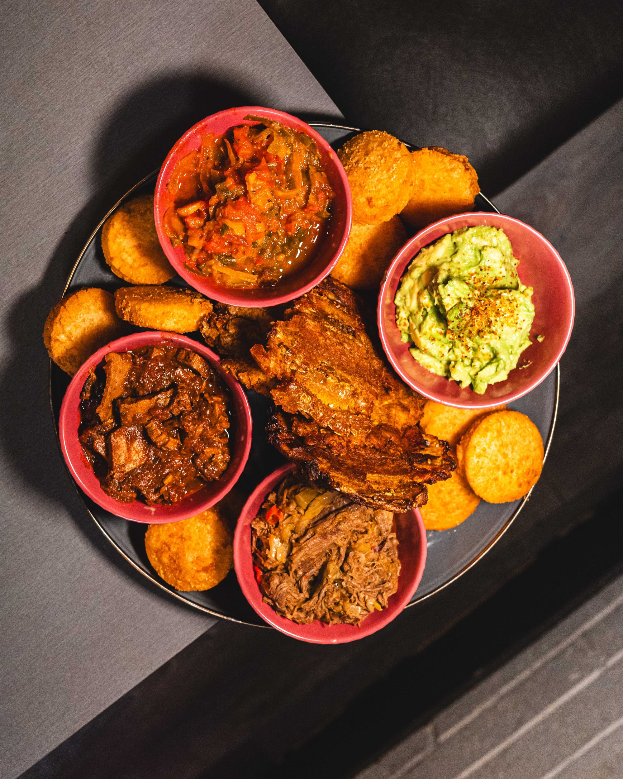Top down shot of plate with fried plantains, mini arepa, pulled beef, vegetables and avocado