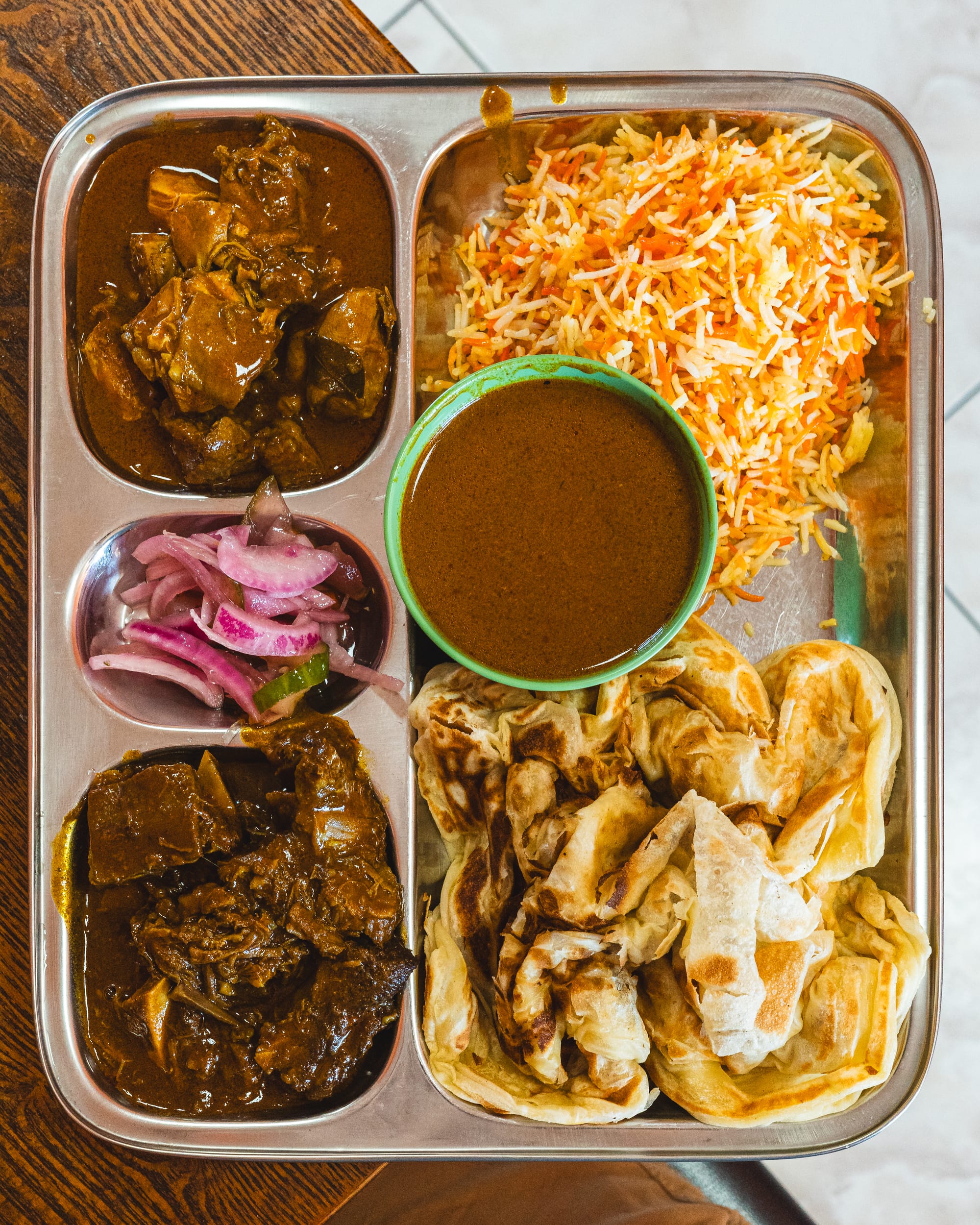 Top down of curry on a silver tray with rice, pickles and roti