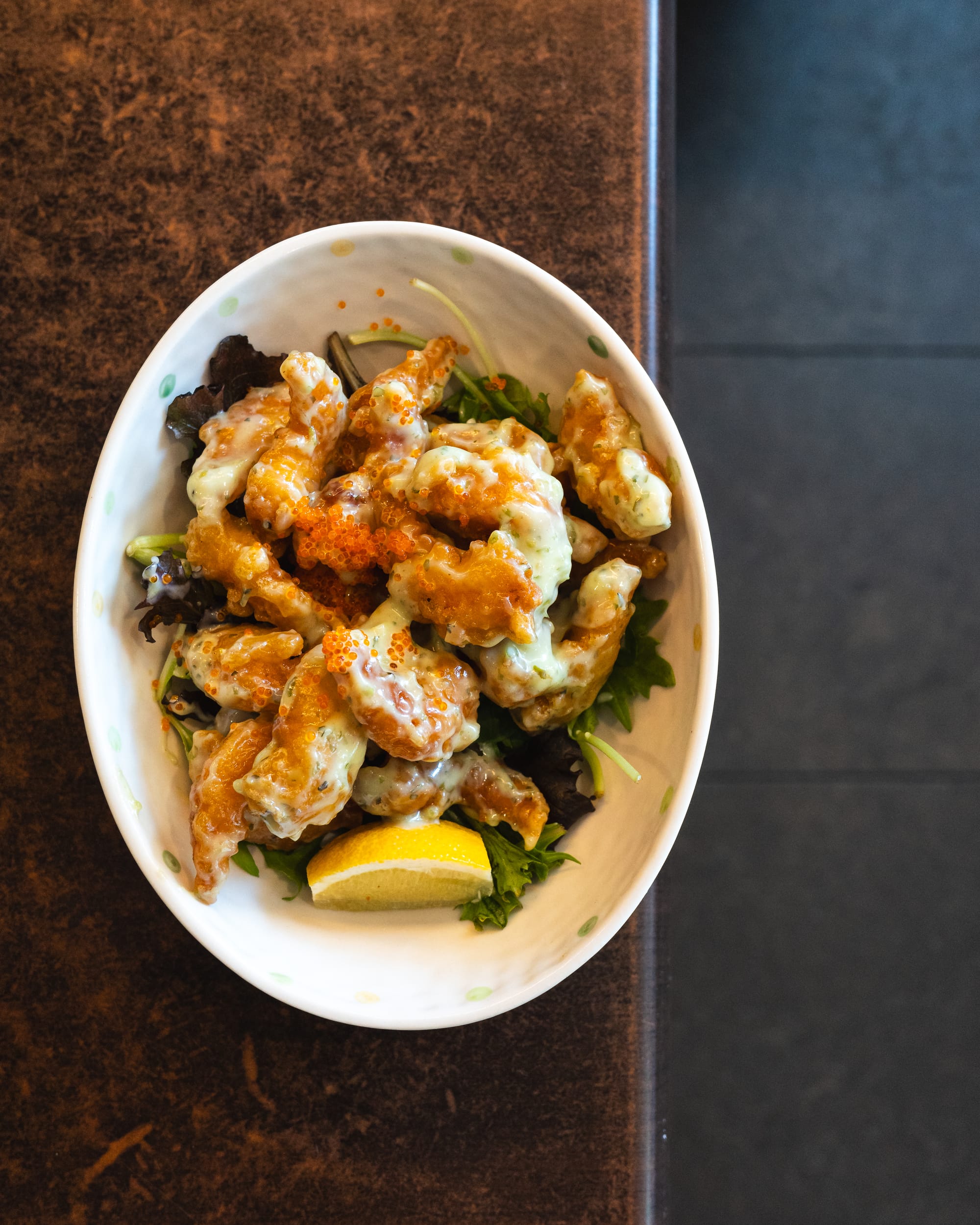 Top down of fried prawn in wasabi mayonnaise sauce with salad and lemon slice