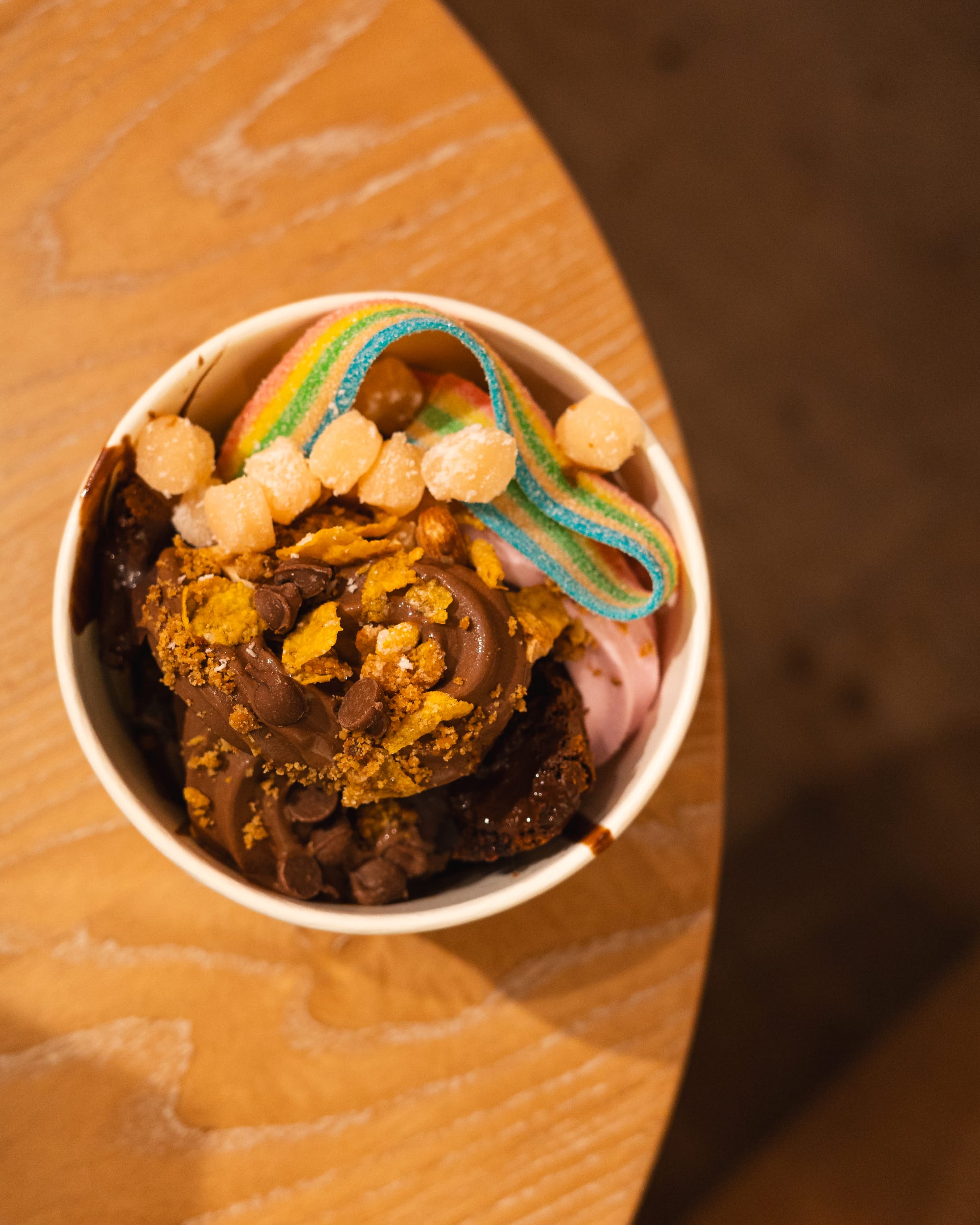 Top down shot of chocolate and strawberry froyo with a sour strap, jellies, choc chips and corn flakes