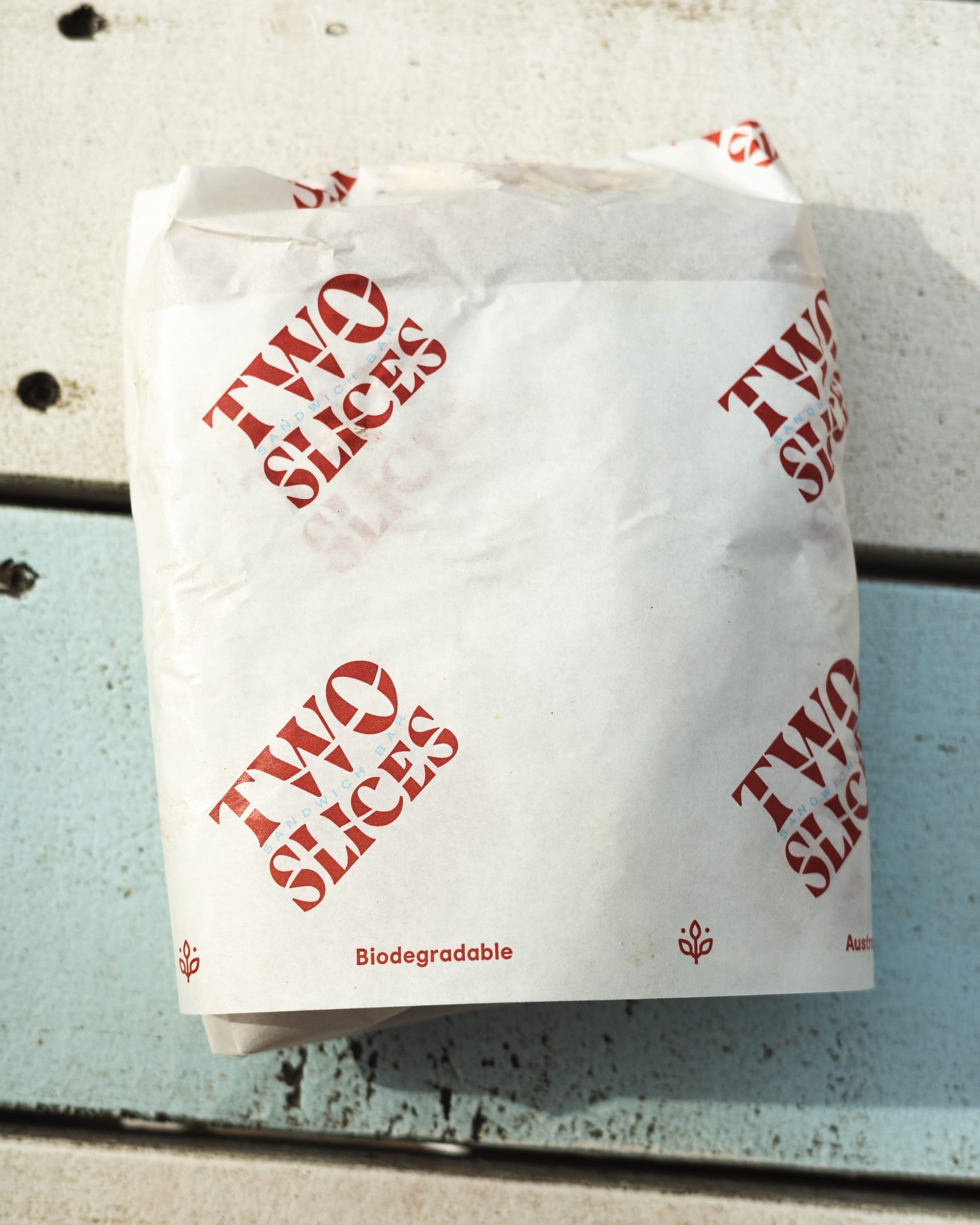 Close up of sandwich wrapped in paper with the words "Two Slices"