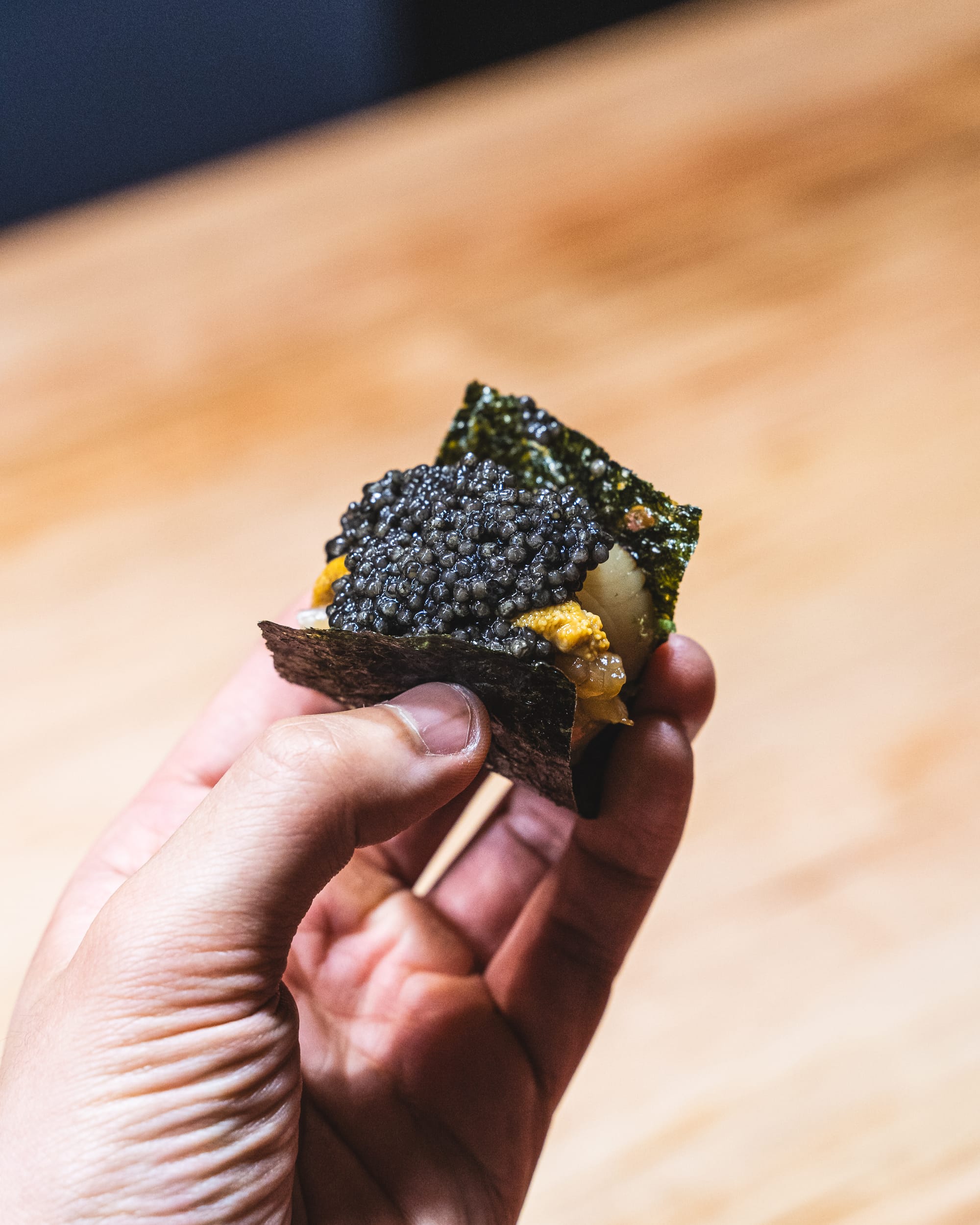 Close up of hand holding seaweed with cucumber, uni and caviar