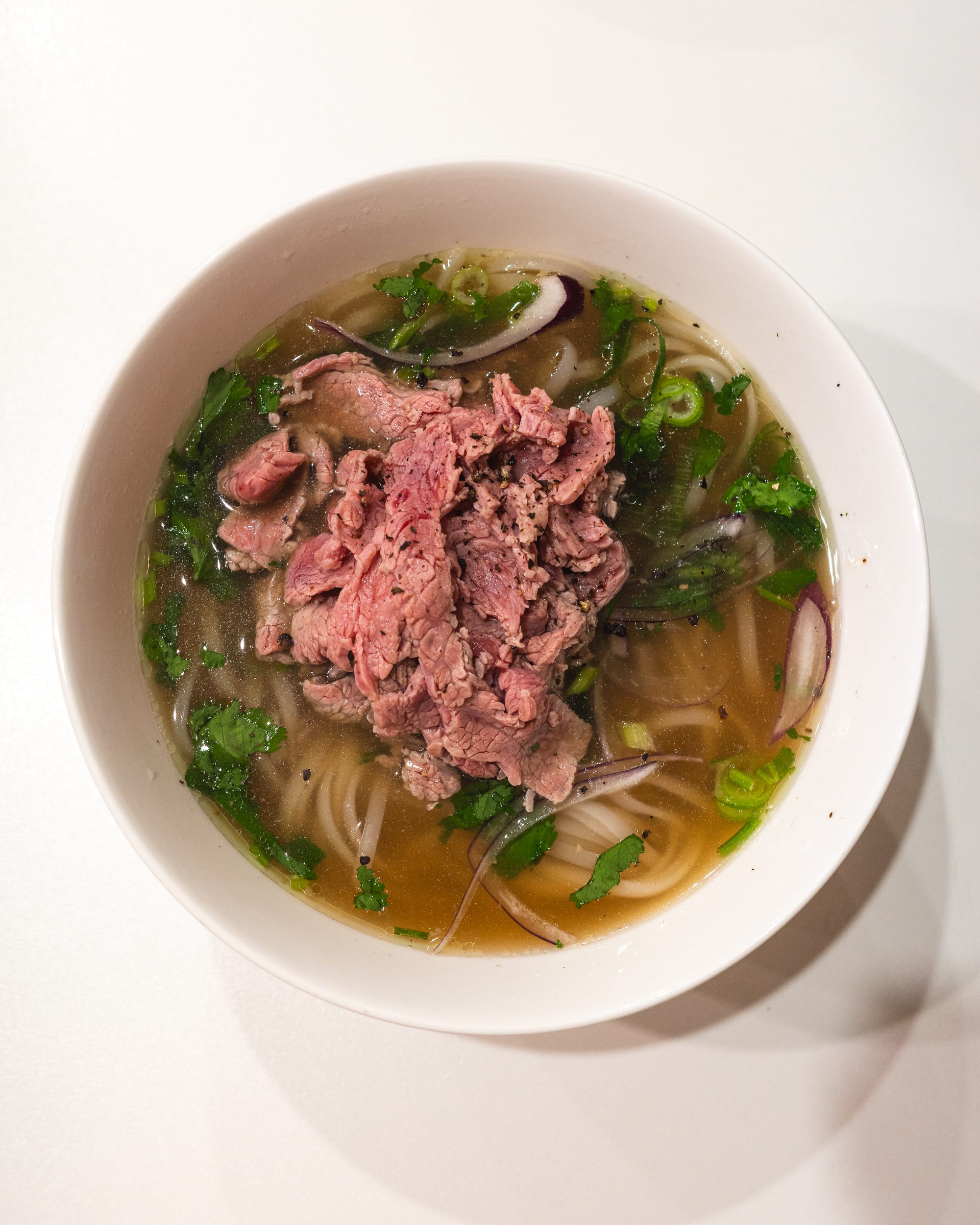 Top down shot of pho showing raw beef, noodles, spring onions, garnish and onion