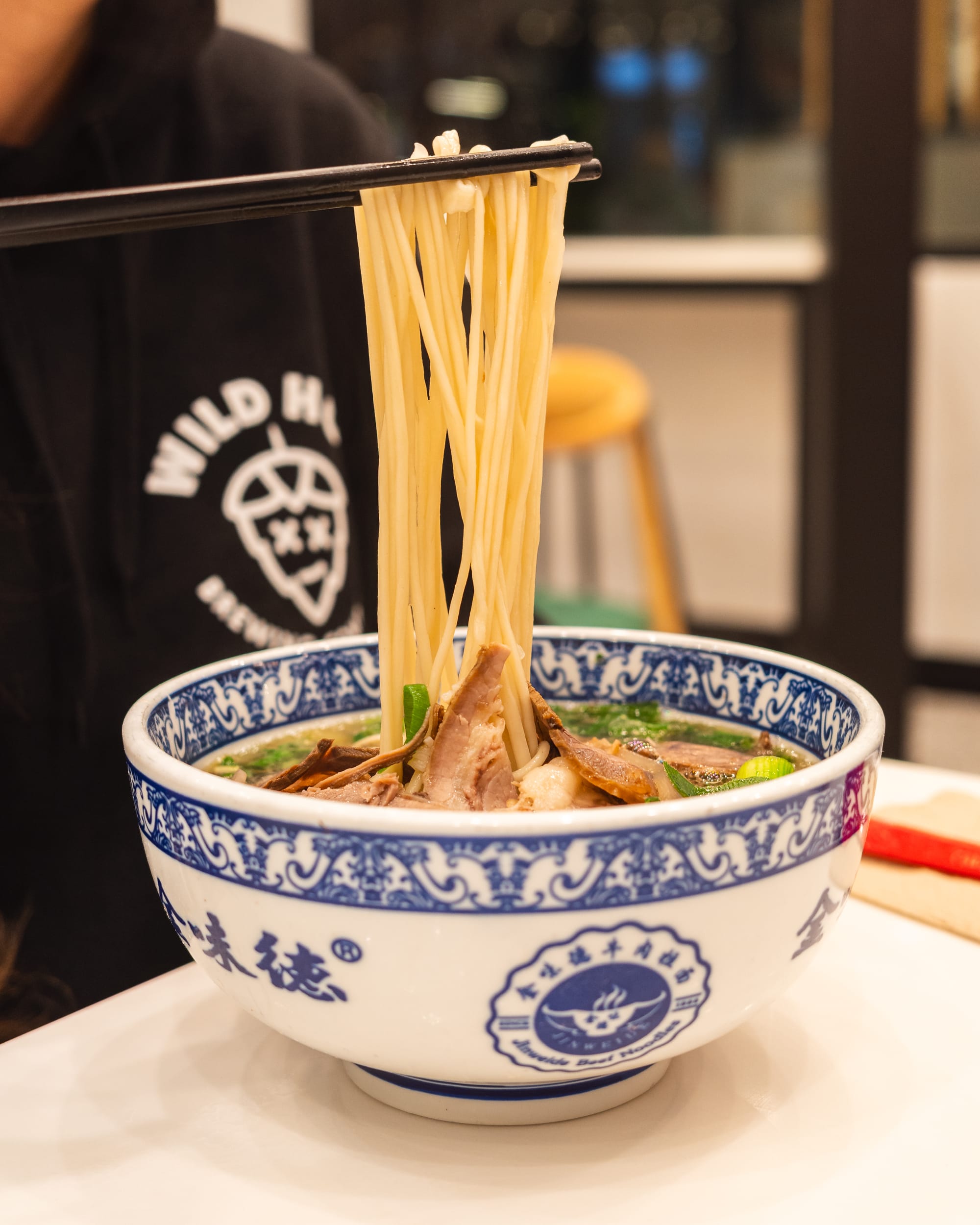 Close up of noodles in a bowl being lifted up by chopsticks