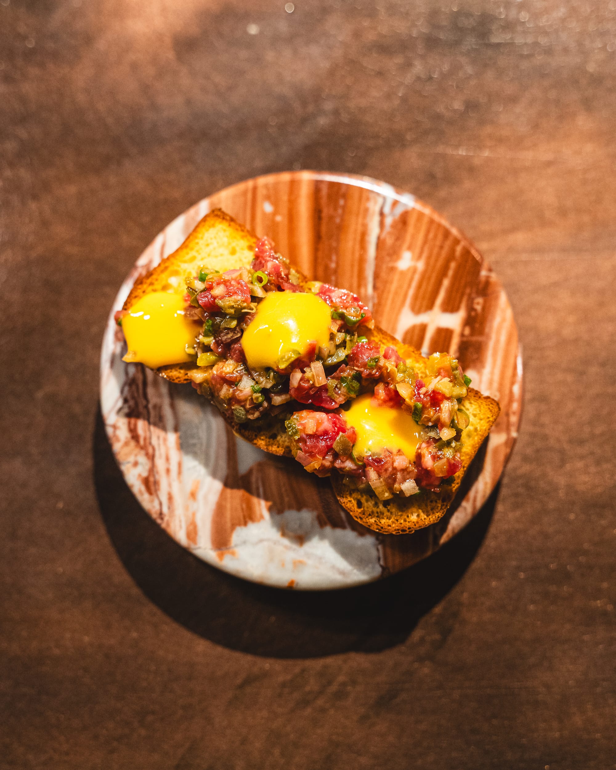 Top down shot of beef tartare served on top of brioche with egg yolk