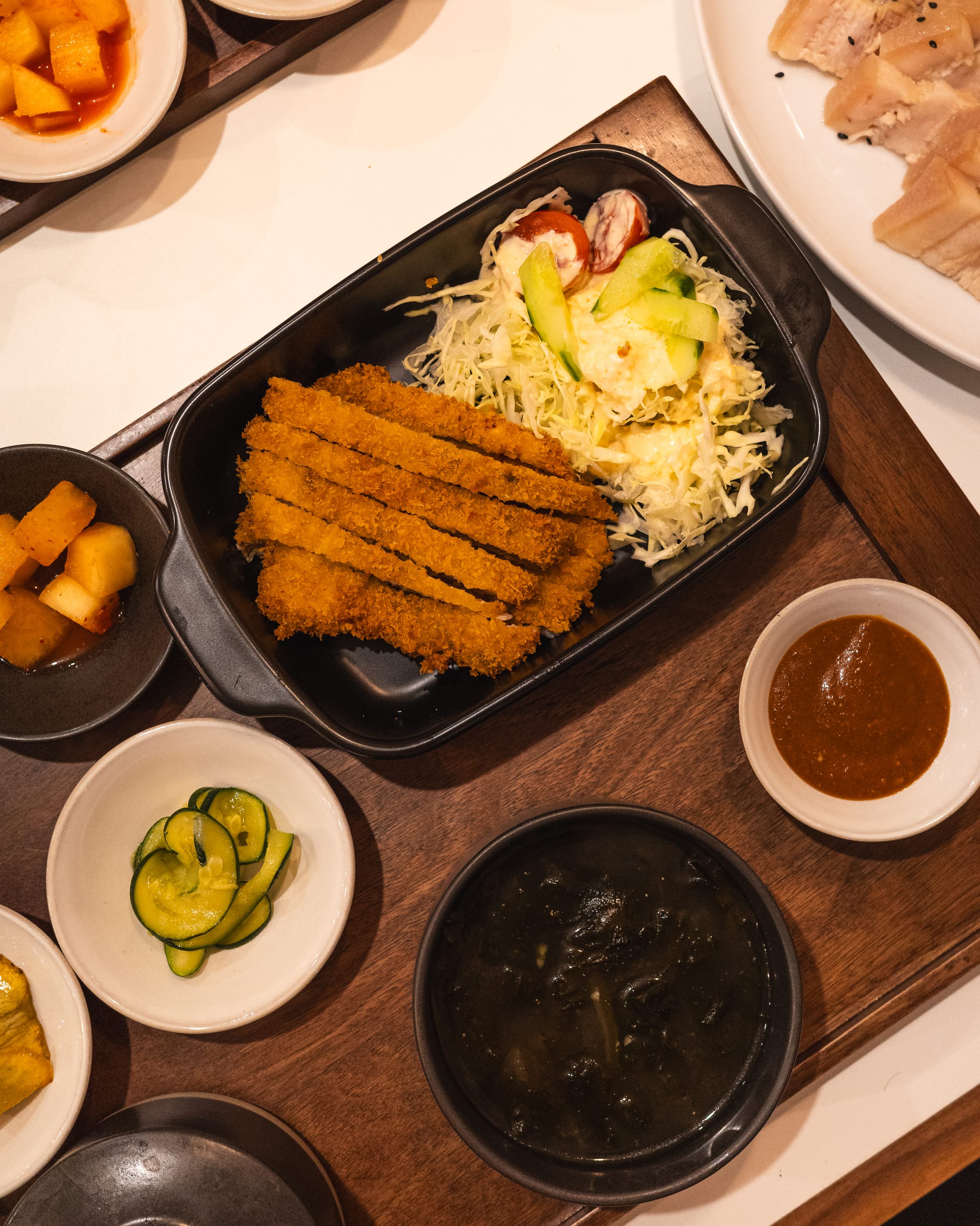 Top down shot of pork cutlet with a side of seaweed soup, zucchini and pickled raddish 