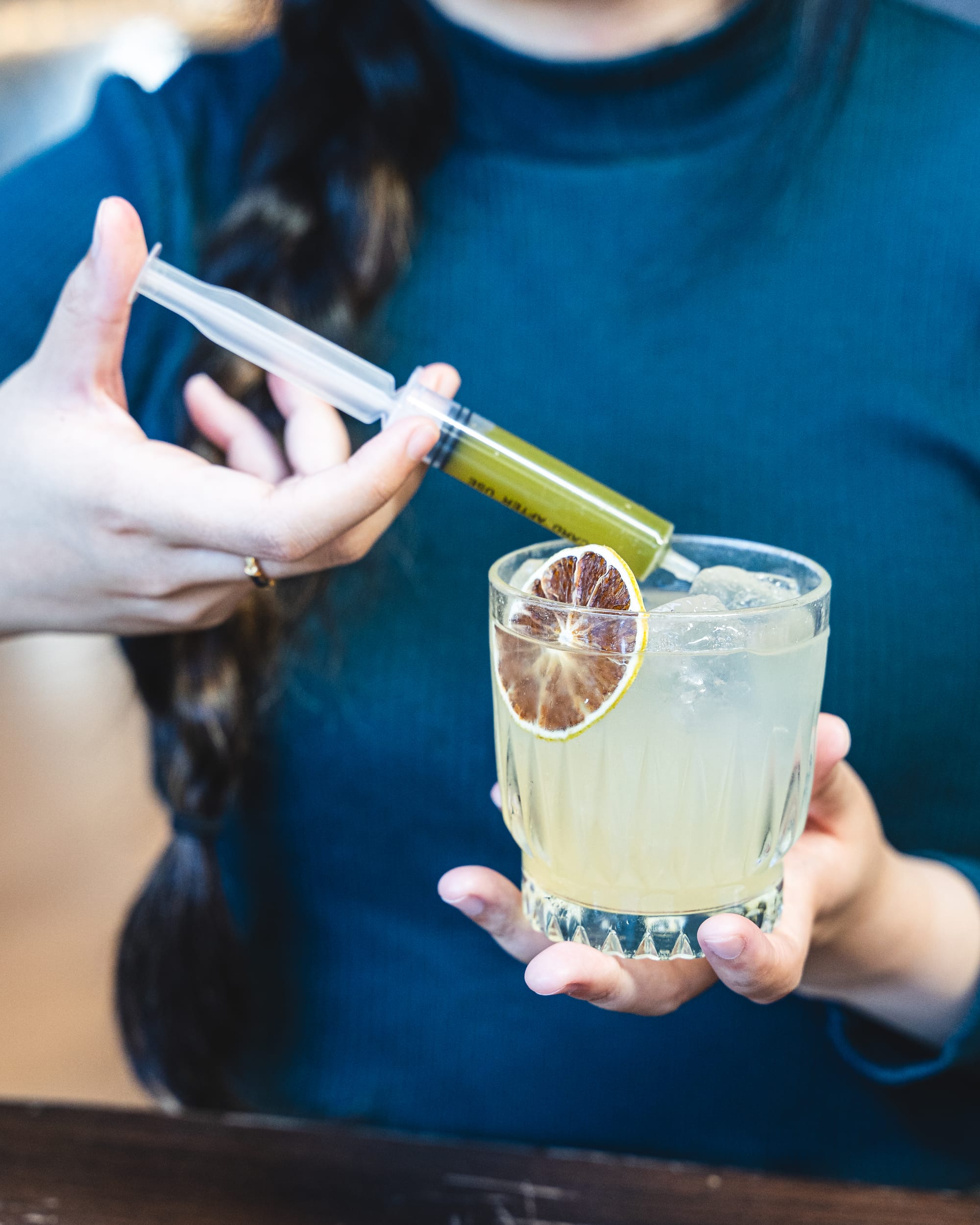 Hand holding margarita cocktail with syringe with green liquid