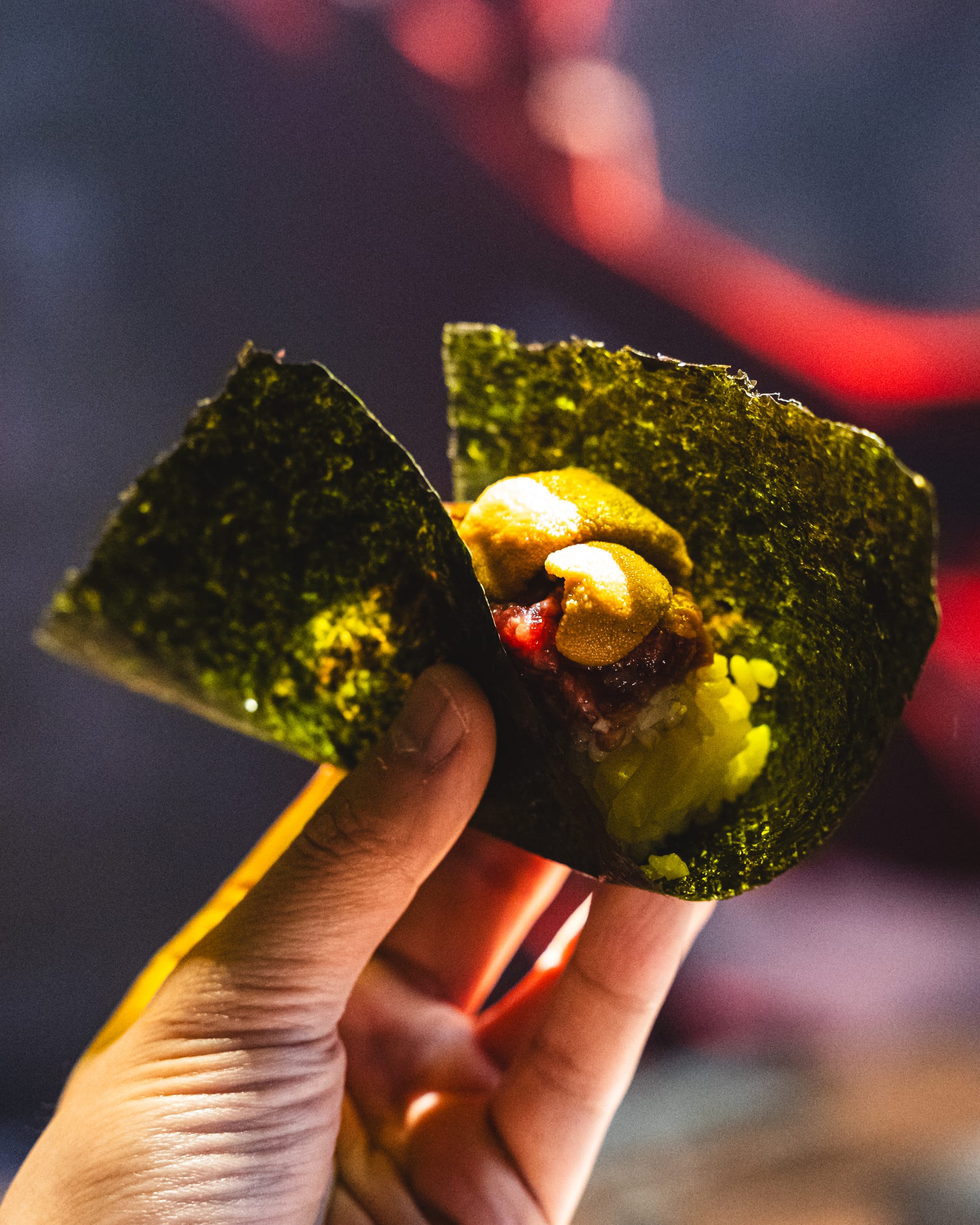 Hand holding sushi rice, uni and wagyu wrapped in seaweed