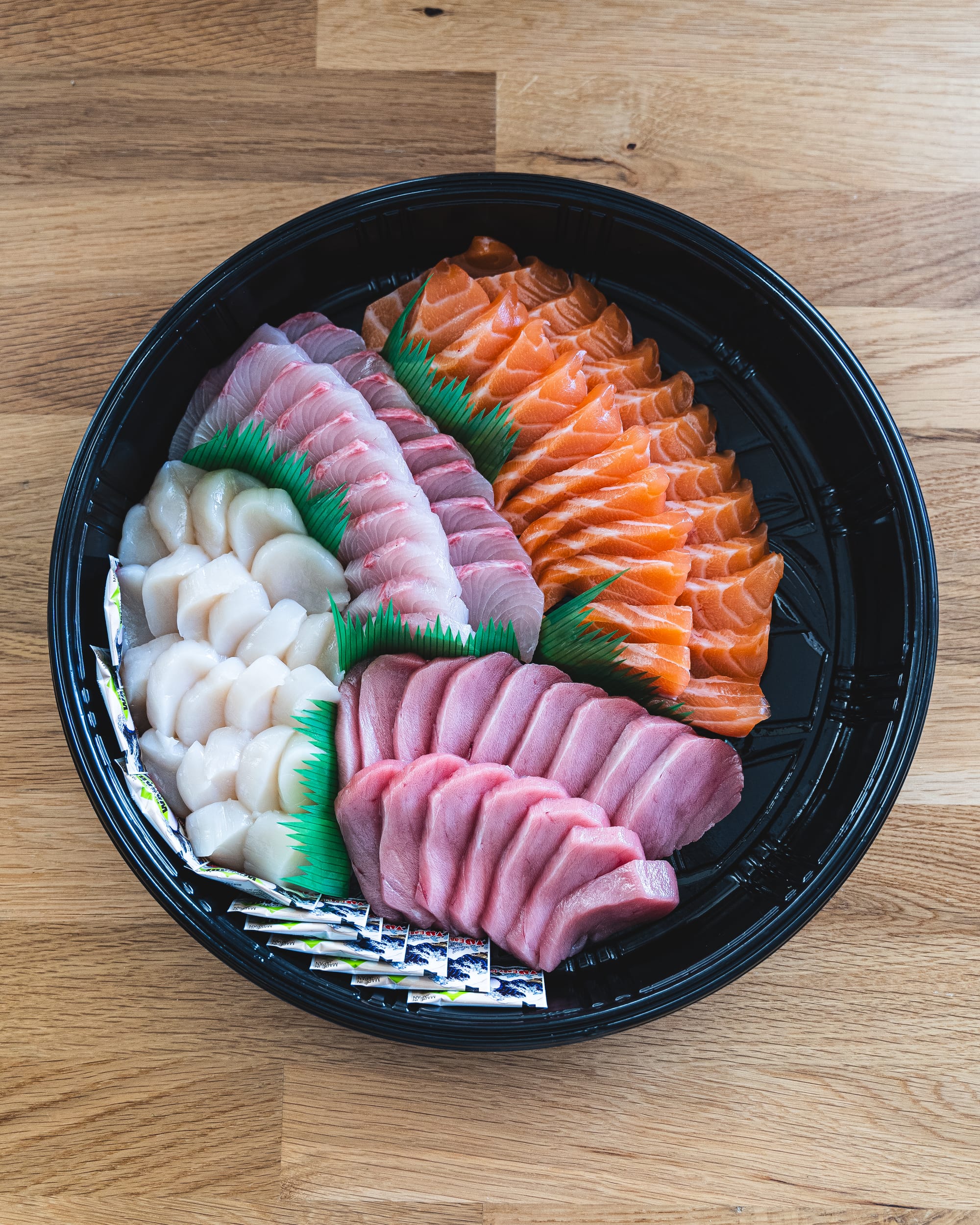 Close up of scallop, whitefish, salmon and tuna sashimi in circular plastic tray