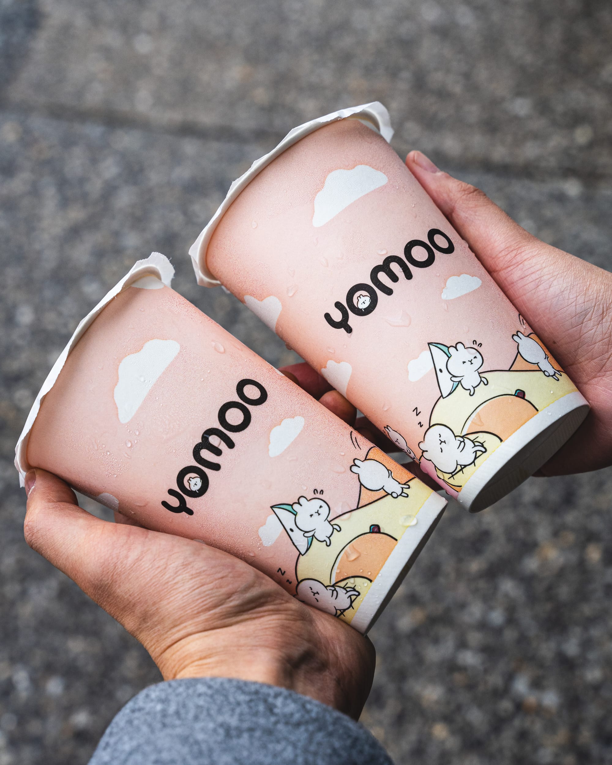 Hands holding two paper cups with YoMoo branding