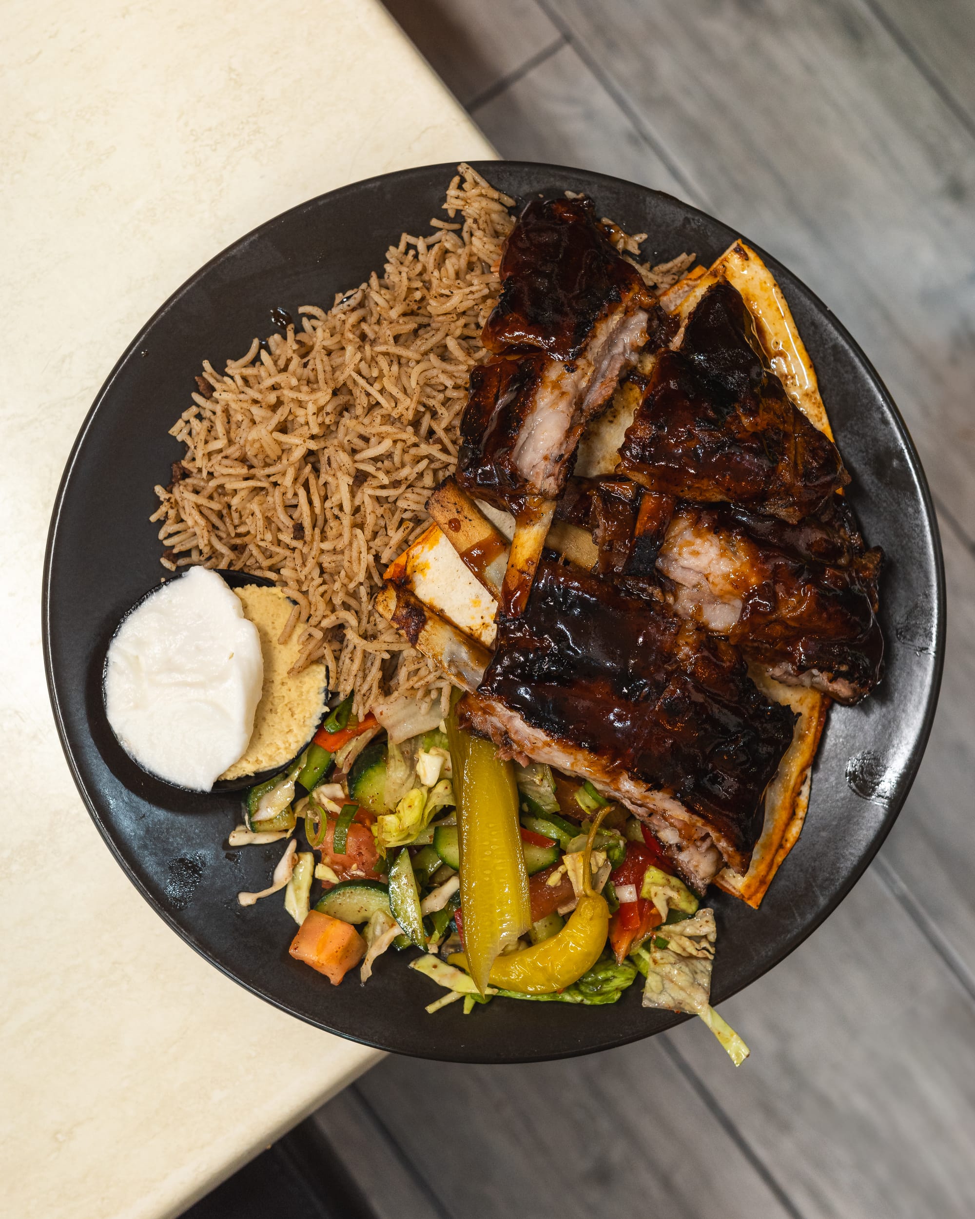 Top down shot of plate with garlic sauce, hummus, vegetables, briyani rice and lamb ribs