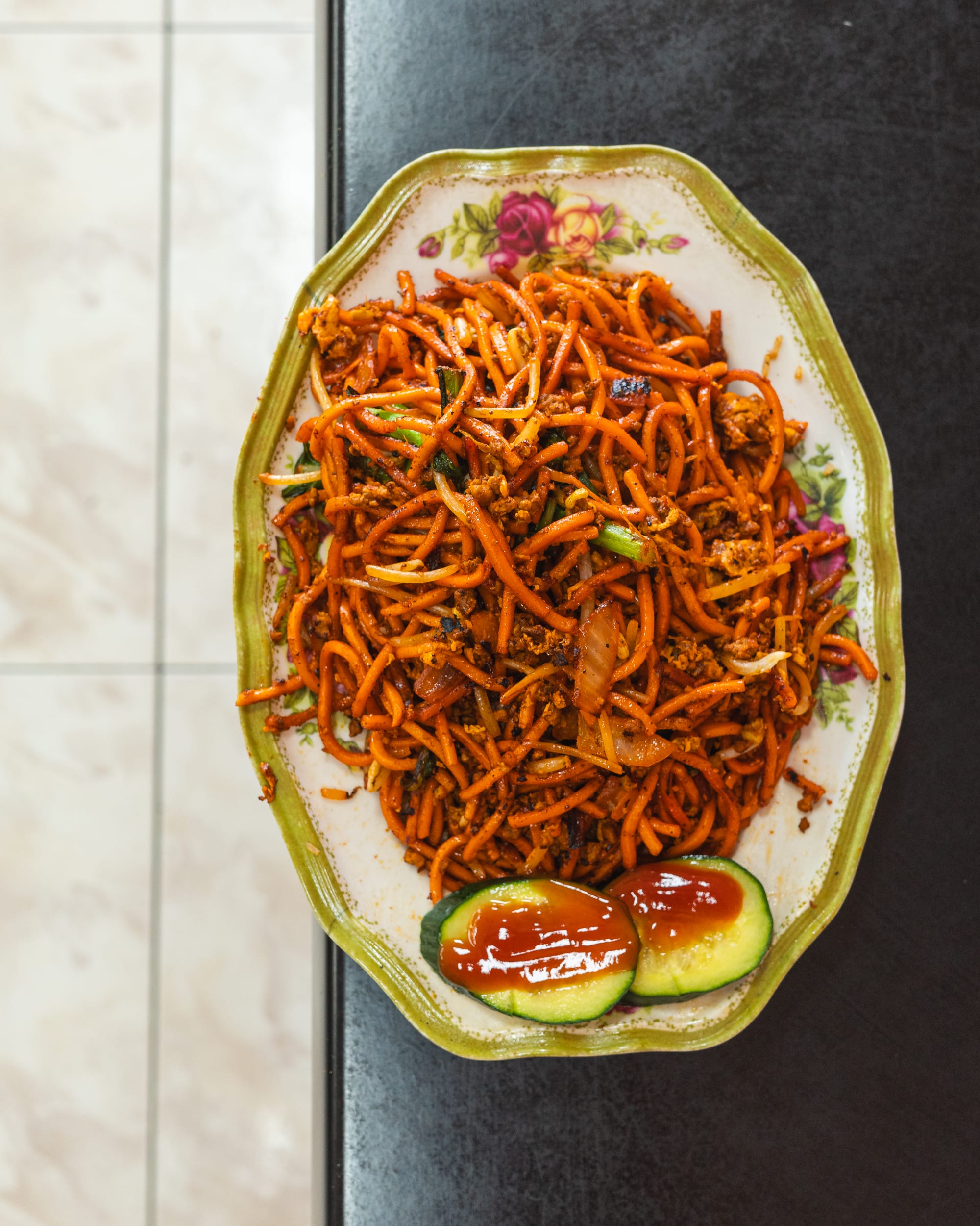 Top down shot of fried mee goreng with cucumber and tomato sauce