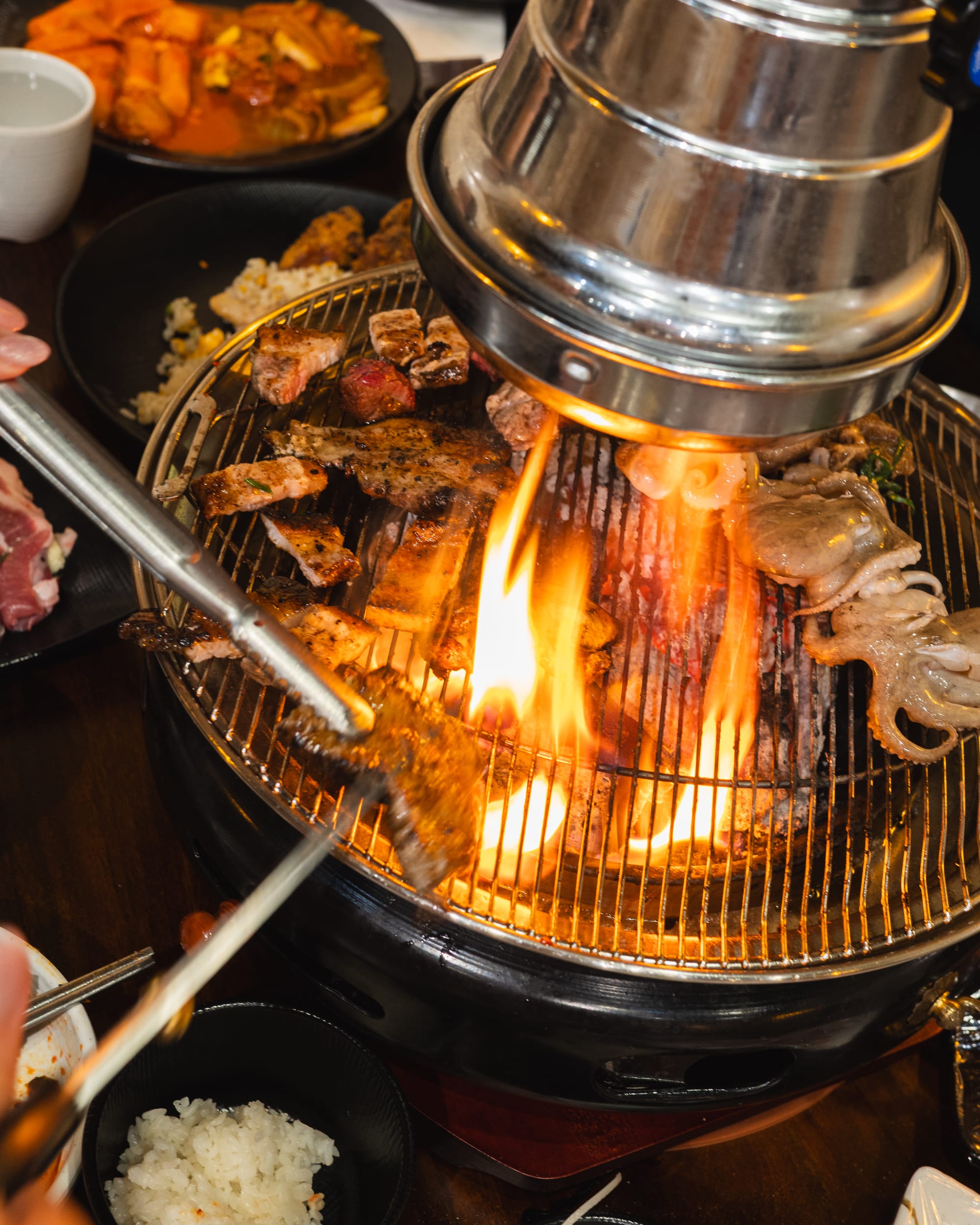 KBBQ meats being cooked on a charcoal grill and being cut