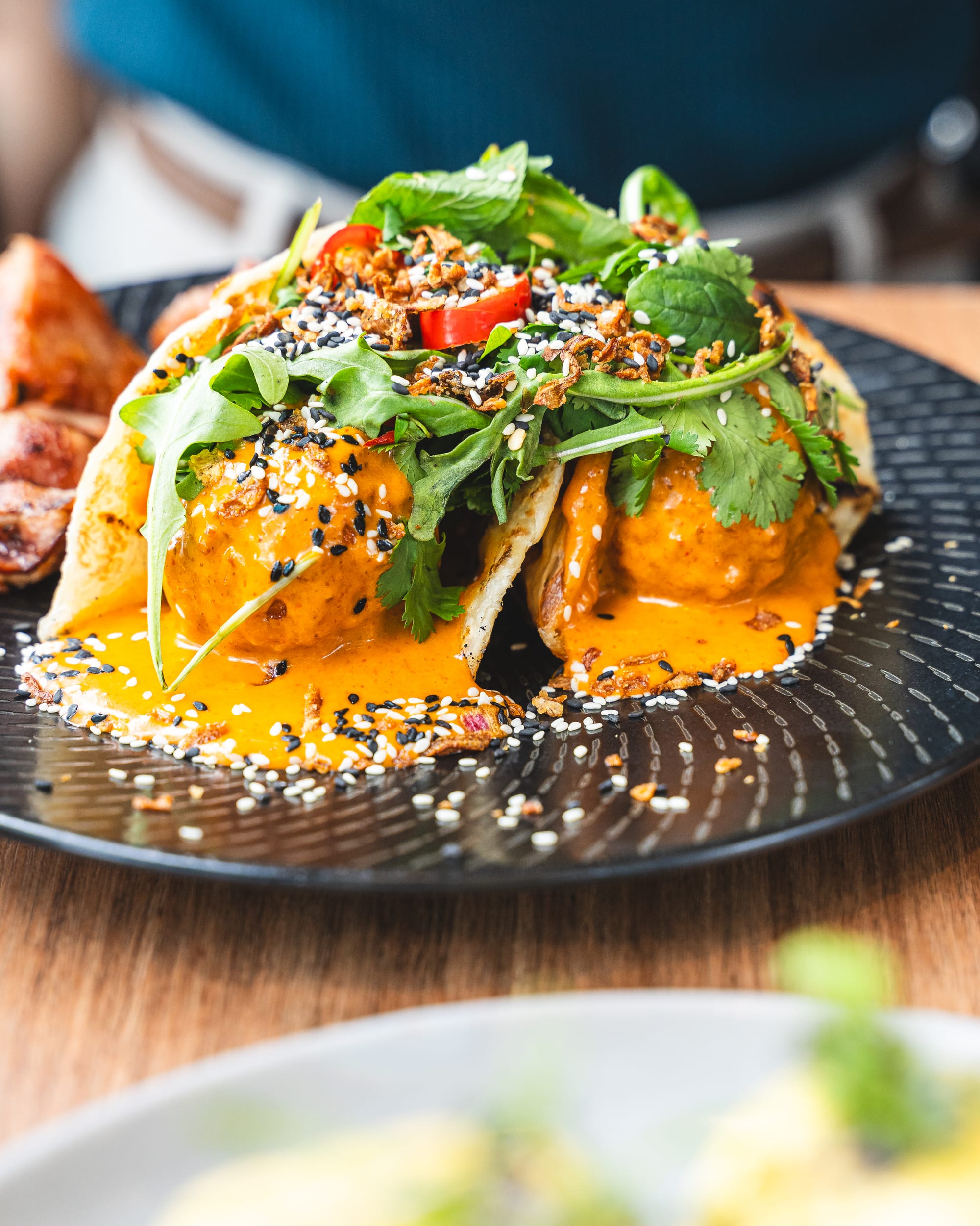 Close up of deep fried eggs in roti garnished with greens and chilli and sesame seeds