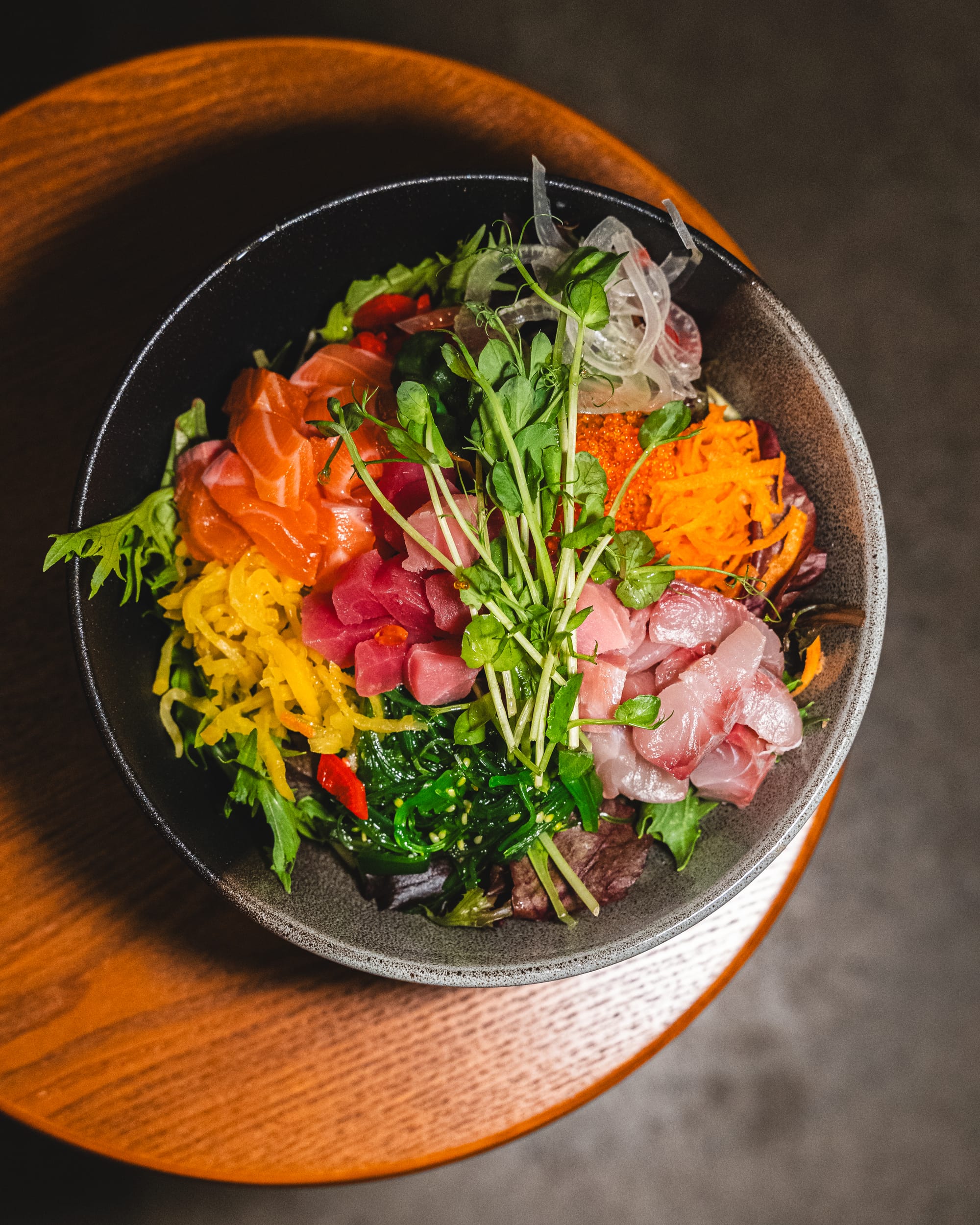 Top down shot of sashimi bowl with cubed tuna, yellowtail, salmon and vegetables