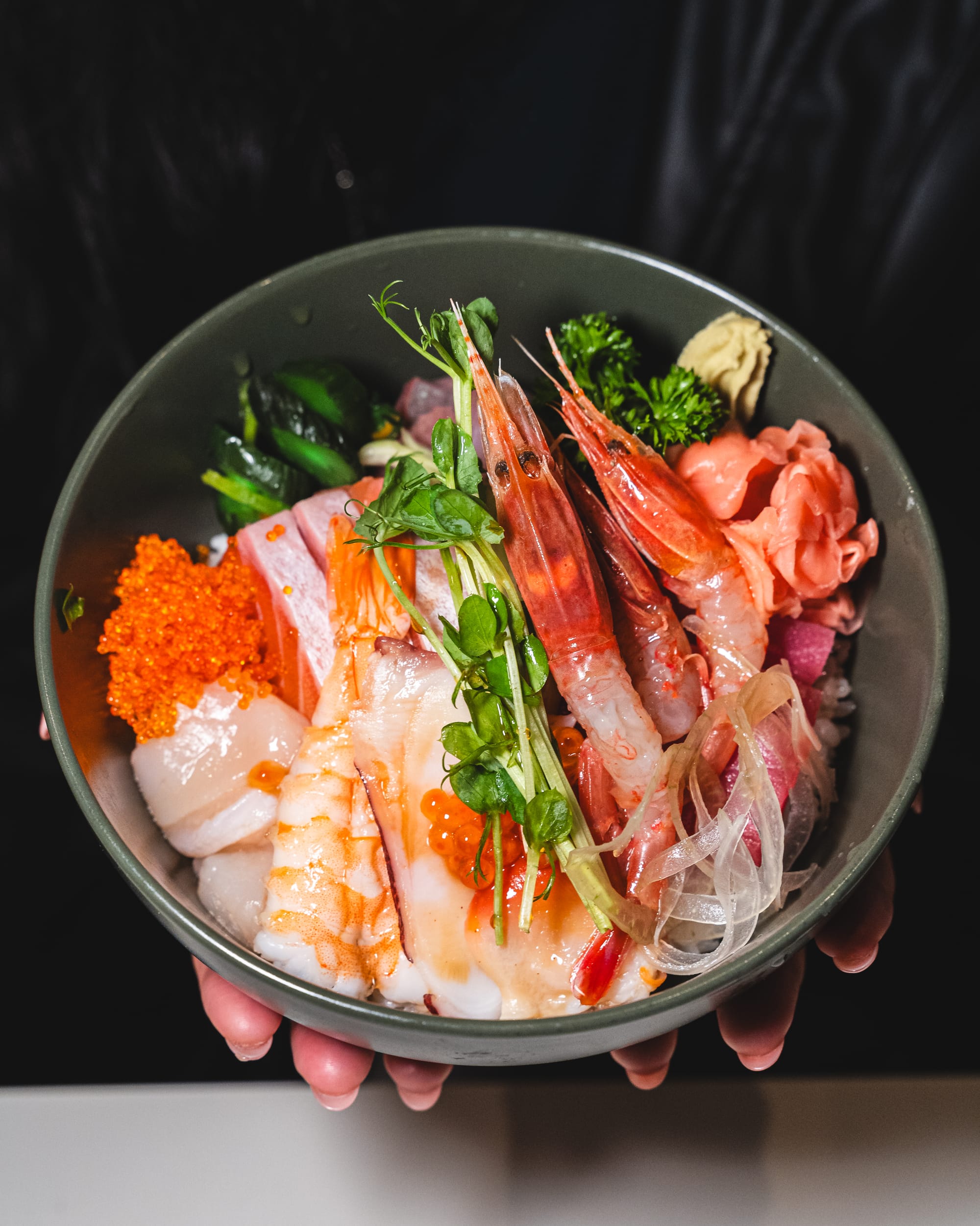 Hand holding sashimi bowl with amaebi, prawn, scallop and tobiko