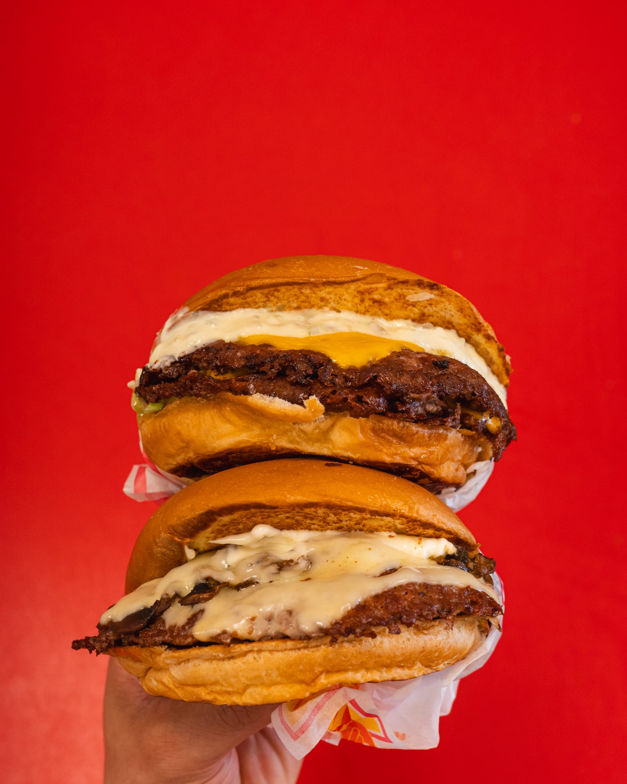 Hands holding burgers against a red background