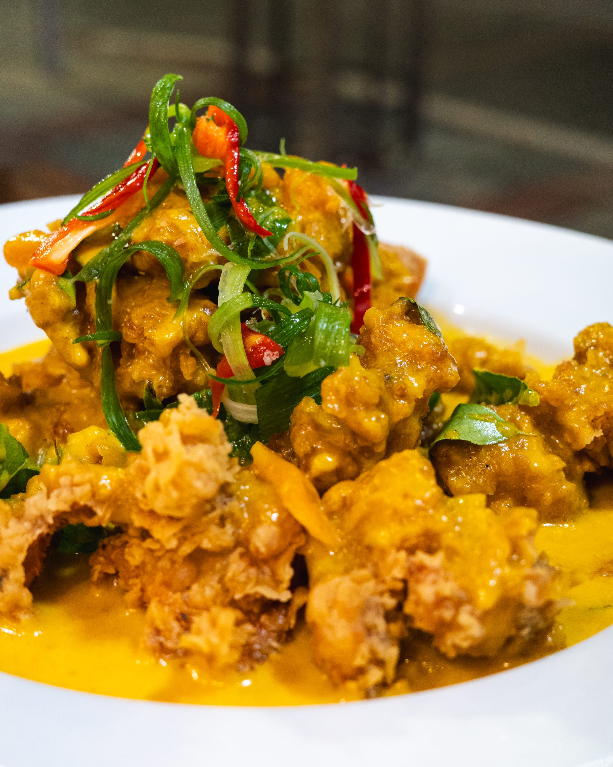 Close up of fried chicken in a salted egg yolk sauce, topped with spring onions and chilli