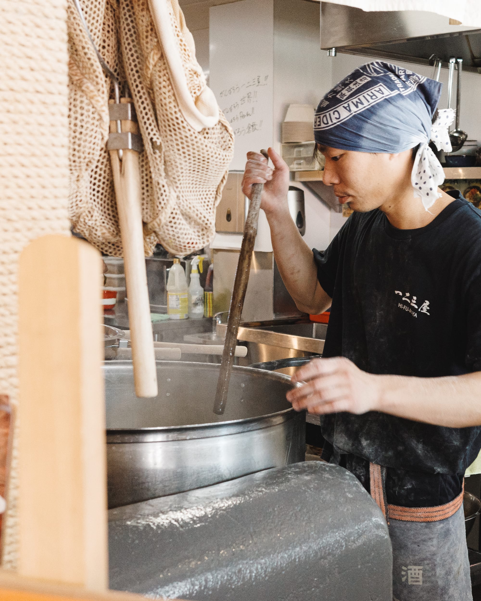 Man stirring large pot of water with a wooden rod